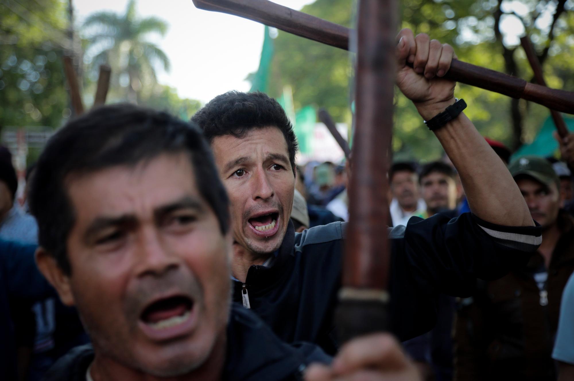 En imagen del jueves 21 de marzo de 2019, agricultores alzan palos y lanzan consignas contra el gobierno del presidente Mario Abdo Benítez durante la marcha anual de la Federación Nacional Campesina en demanda de más tierras y apoyo del gobierno, en Asunción, Paraguay.