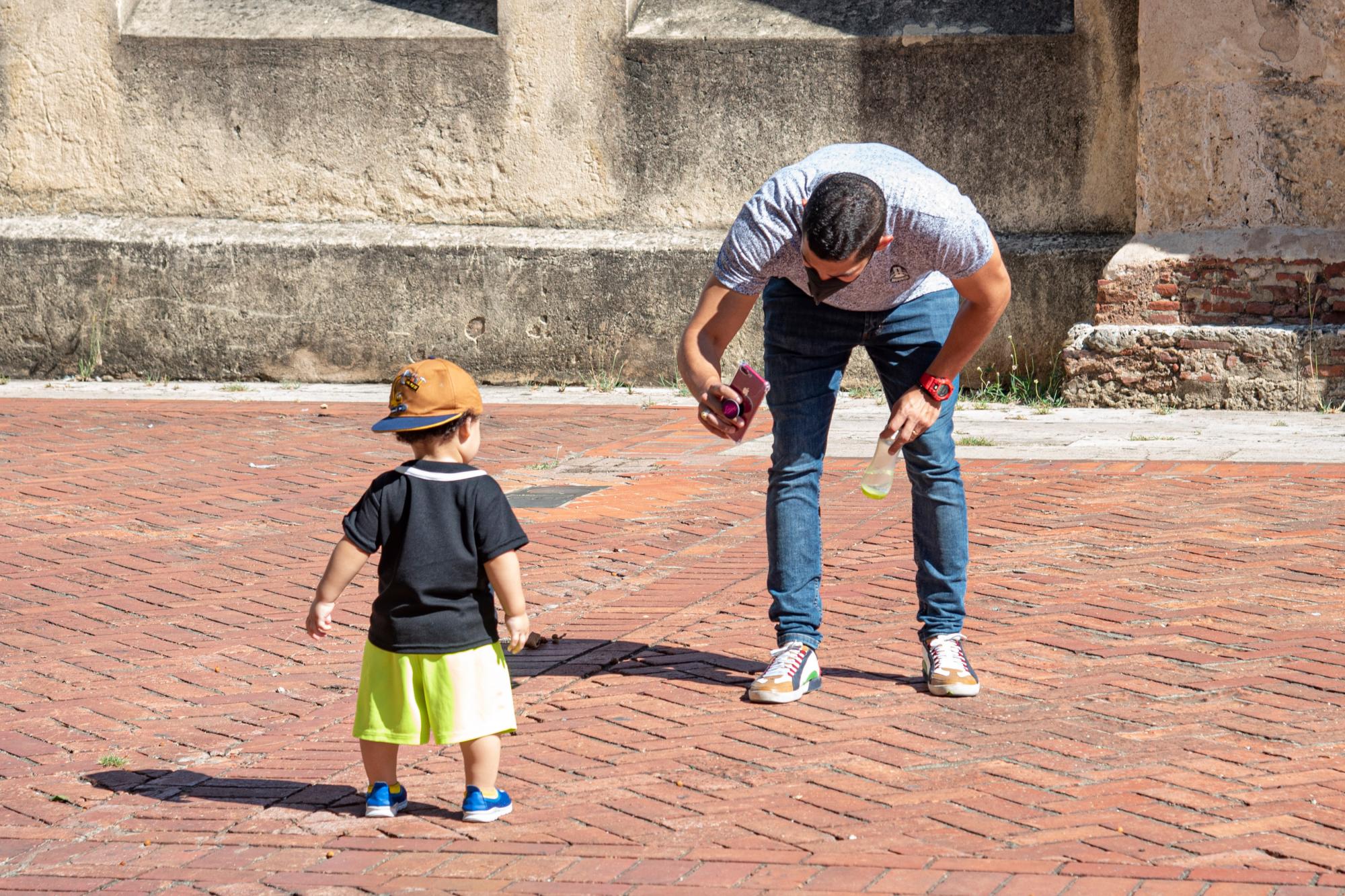 Padre toma foto a su hijo con su celular en el parque Colón, Ciudad Colonial.