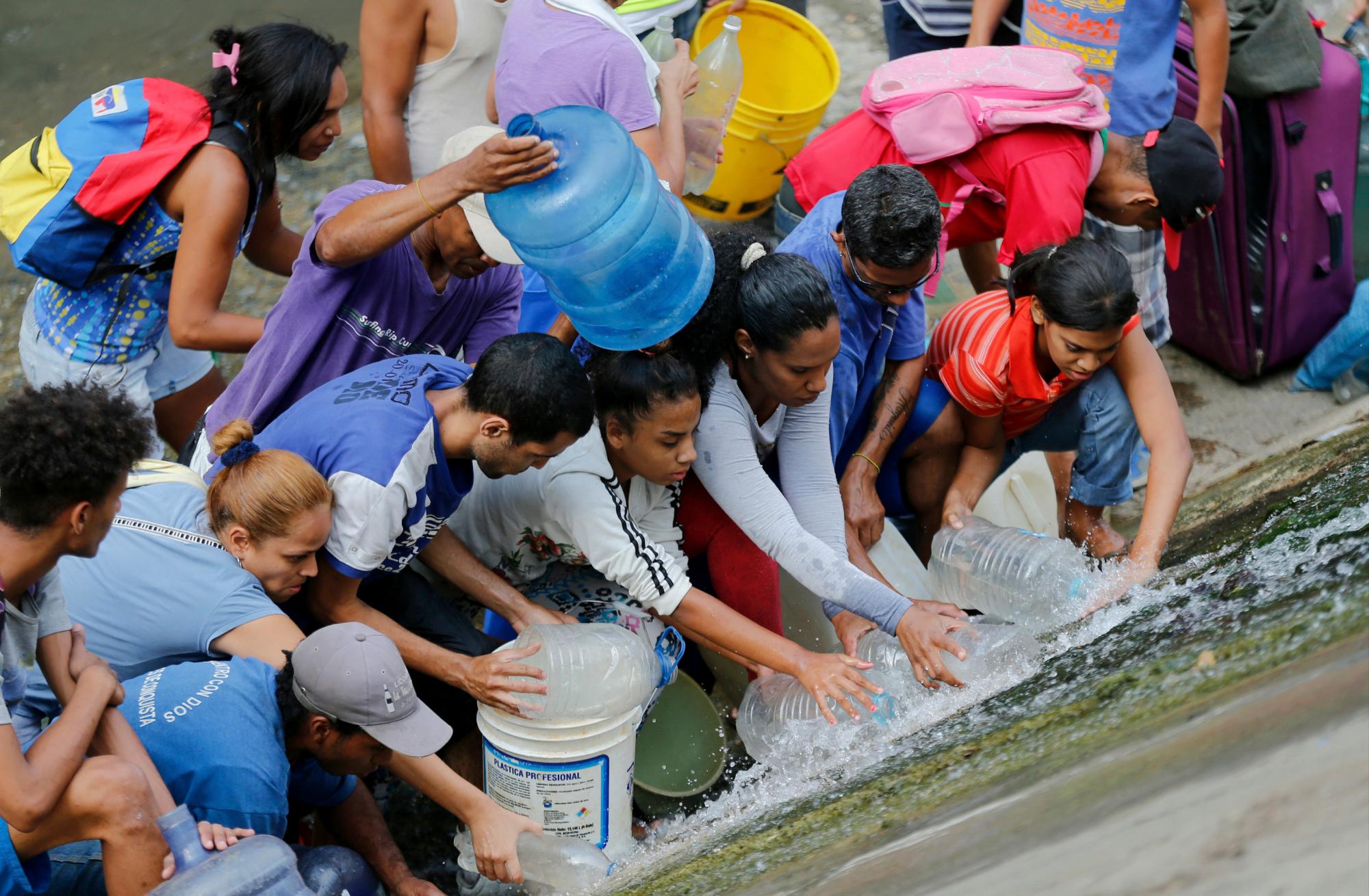 Personas recogen agua que cae de una tubería con fugas a lo largo de las orillas del río Guaire durante los apagones ondulantes, lo que afecta el acceso al agua corriente en Caracas, Venezuela. 