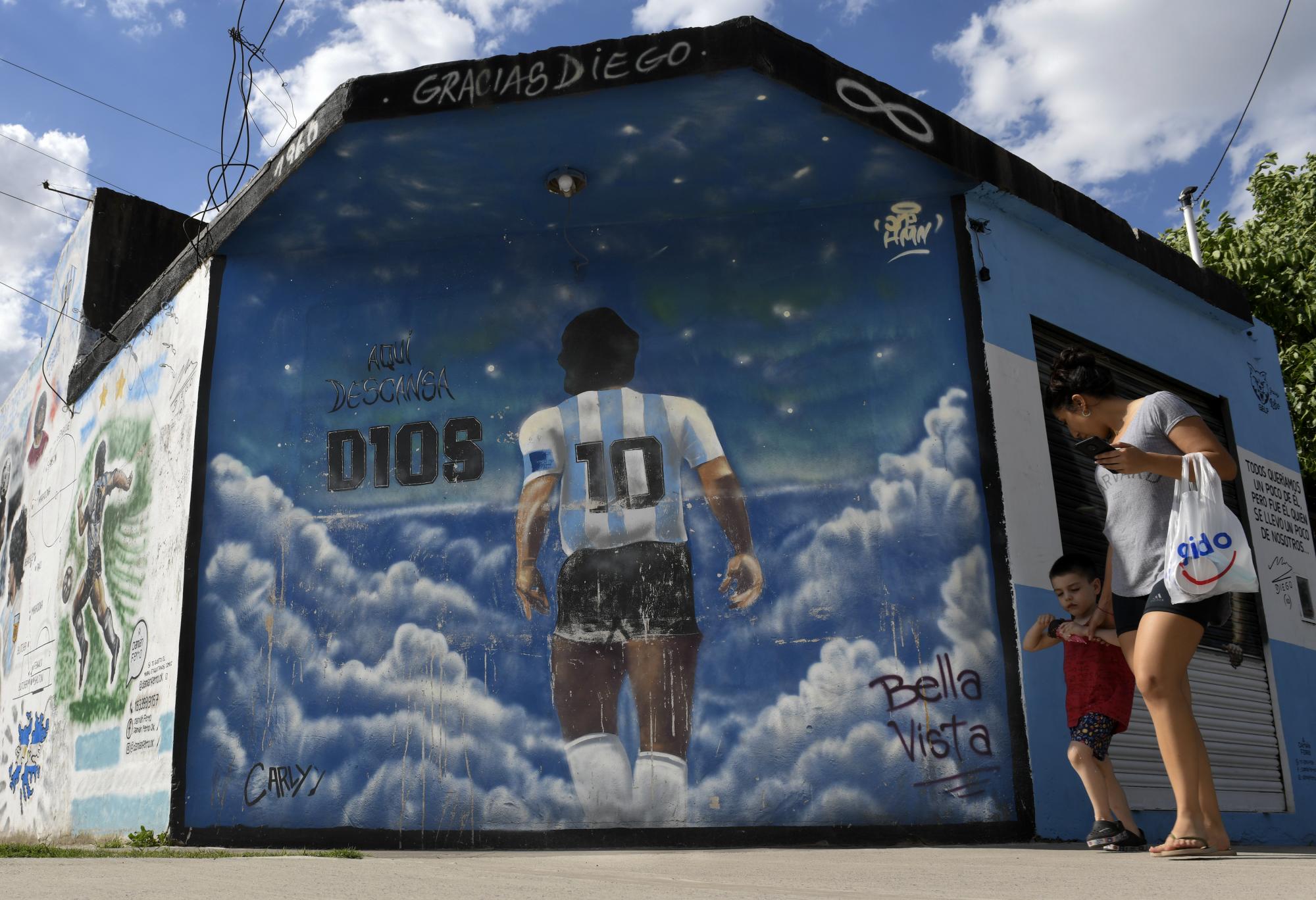 Una mujer y un niño pasan caminando frente a un mural que muestra a Diego Mardona de espaldas en el barrio Lomas de Marilo, en Buenos Aires, el 22 de noviembre del 2021. El 25 de noviembre se cumple el primer aniversario de la muerte del astro. (AP/Gustavo Garello)