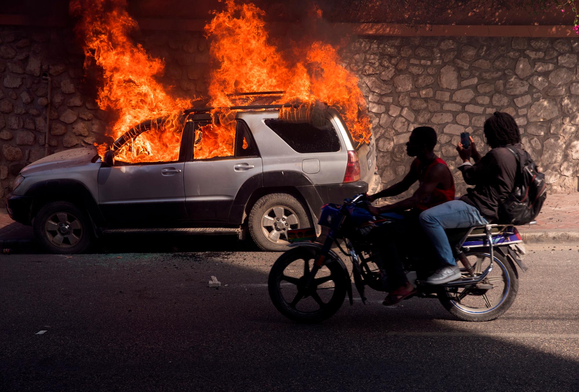 PUERTO PRÍNCIPE (HAITÍ), 14/02/2021.- Fotografía de un automovil ardiendo durante una jornada de protesta contra el Gobierno de Jovenel Moise hoy, en la zona de Delmas, en Puerto Príncipe (Haití). Una nueva crisis política estalló en Haití la semana pasada tras la destitución de tres magistrados por decreto del presidente Jovenel Moise, lo que ha elevado las alertas de la comunidad internacional. EFE/ Orlando Barría 
