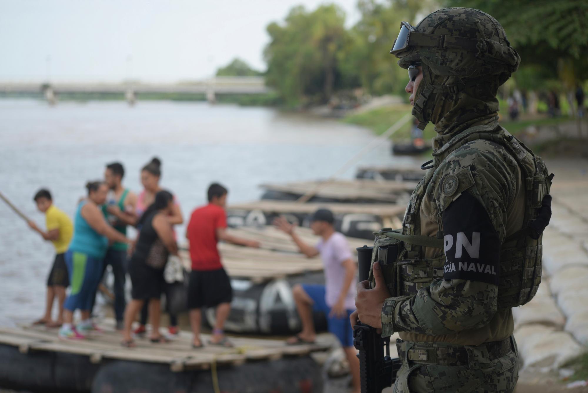 Un marine mexicano hace guardia en el río Suchiate, vigilando a los migrantes que cruzan de Guatemala a Ciudad Hidalgo, mientras los lugareños se paran en una balsa en México, el domingo 16 de junio de 2019. México enfrenta una mayor presión de Estados Unidos para reducir la oleada de migrantes .