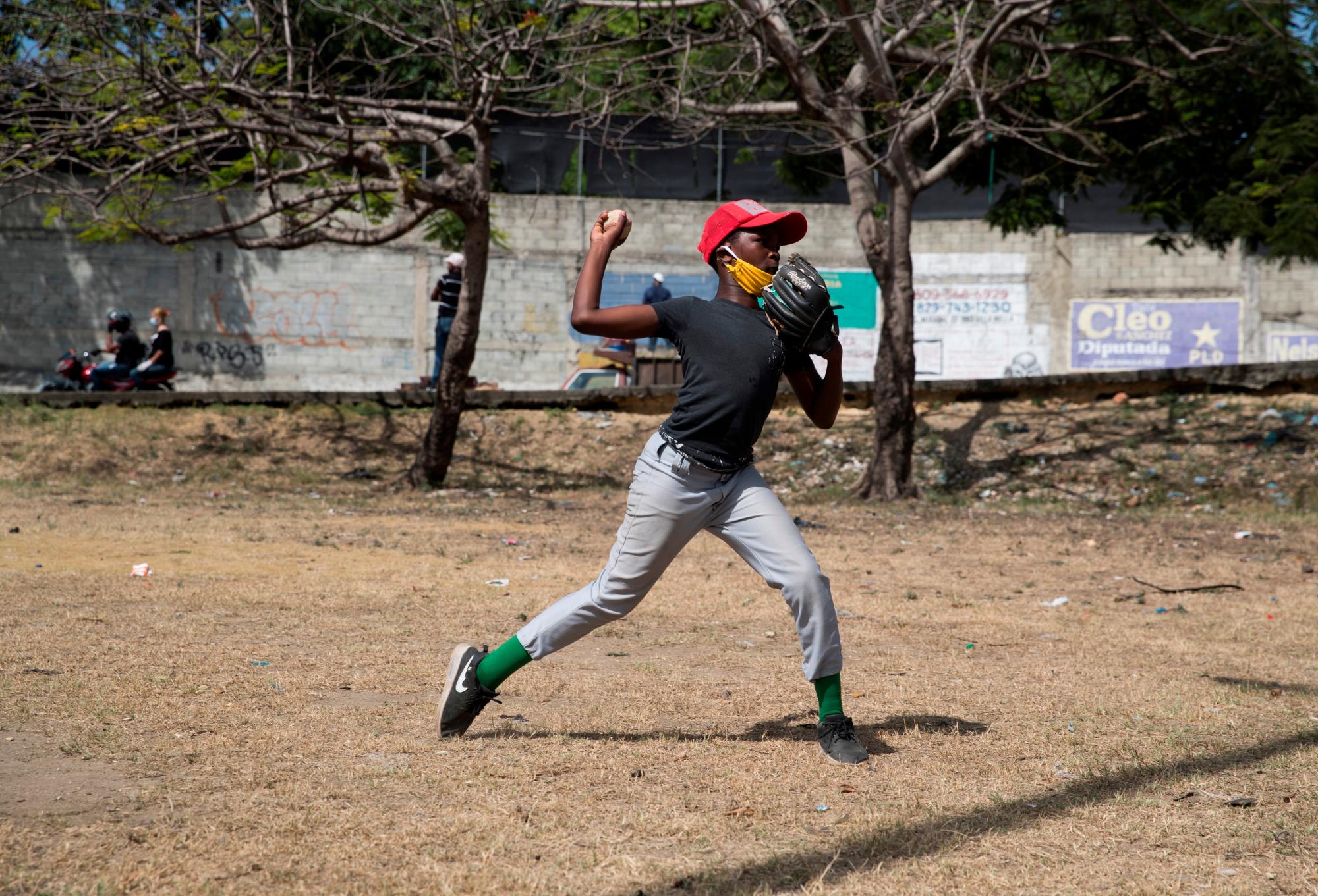 Un joven lanza una pelota durante una practica de béisbol este viernes en un parque en Santo Domingo (República Dominicana). Un batazo tras otro, las pelotas siguen volando en Santo Domingo, una de las principales capitales del béisbol del Caribe. Pero ahora, en tiempos de coronavirus, no vuelan la cerca del play sino que aterrizan en las carreteras o, de vez en cuando, en los faros de un automóvil. Y es que la pandemia ha obligado al béisbol amateur a buscar refugio en las calles, en los descampados, lejos de las canchas, cerradas hace ya dos meses. EFE/Orlando Barría