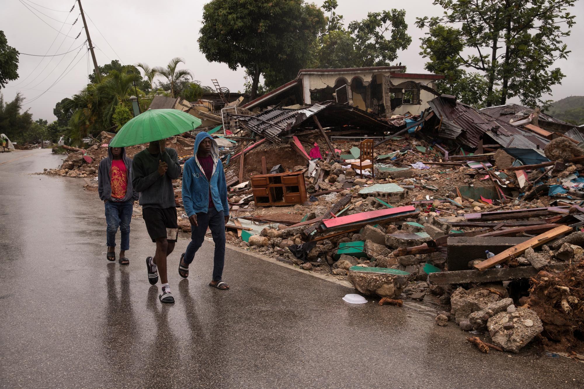 Hombres caminan junto a una casa destruida , mientras cae la lluvia que deja el paso de la tormenta Grace, este martes en Camp Perrin (Haití). Fuertes lluvias cayeron en las últimas horas en el suroeste de Haití, la zona más afectada por el terremoto de magnitud 7,2 en la escala Richter que el sábado pasado causó más de 1.400 muertos y 6.900 heridos. EFE/ Orlando Barría