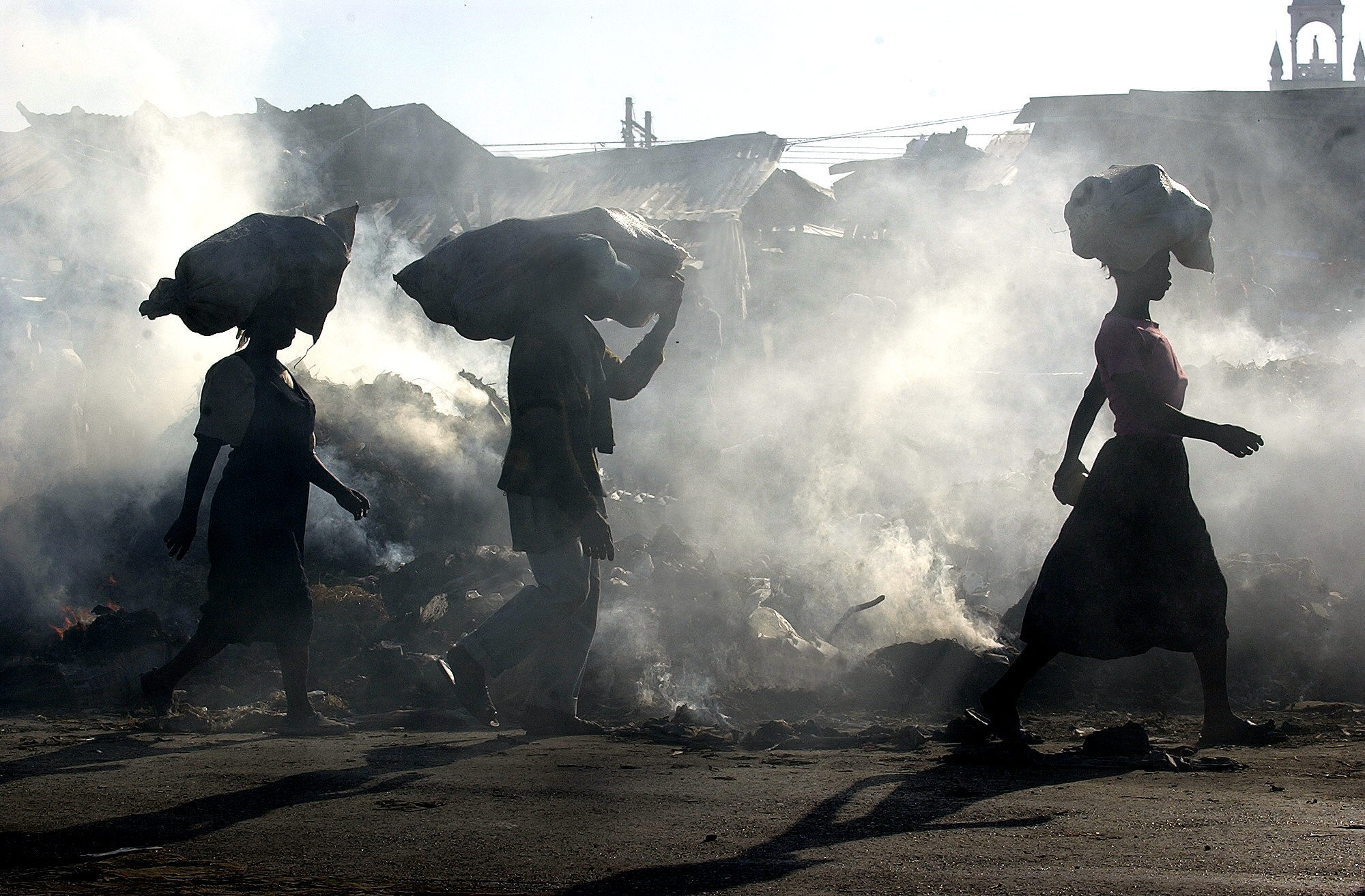PUERTO PRINCIPE (HAITI) 04/02/06.- Haitianos caminan por el mercado de Les Salines, mientras la basura acumulada es quemada en el mismo lugar, lo que produce que todo el mercado este permanentemente cubierto de humo. Las elecciones presidenciales y legislativas del próximo 7 de febrero en Haití se celebrarán bajo la vigilancia de una numerosa fuerza militar de la ONU y en medio de un clima de inseguridad y de violencia. 