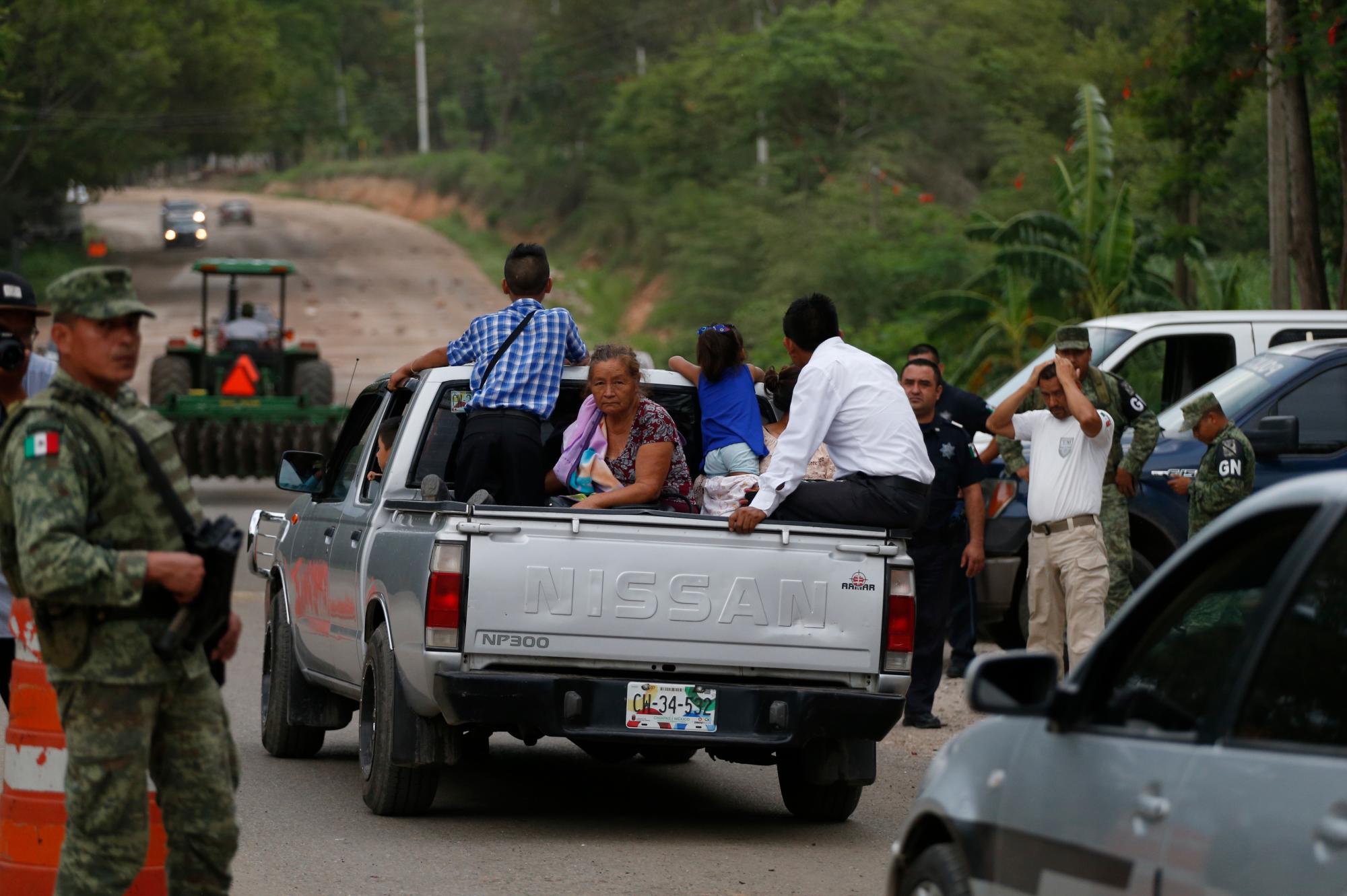 La gente viaja en la parte trasera de una camioneta mientras pasan por un puesto de control de inmigración temporal tripulado por soldados que llevan brazaletes de la Guardia Nacional de México, justo al norte de Ciudad Cuauhtémoc, Estado de Chiapas, México, sábado, 15 de junio de 2019. 
