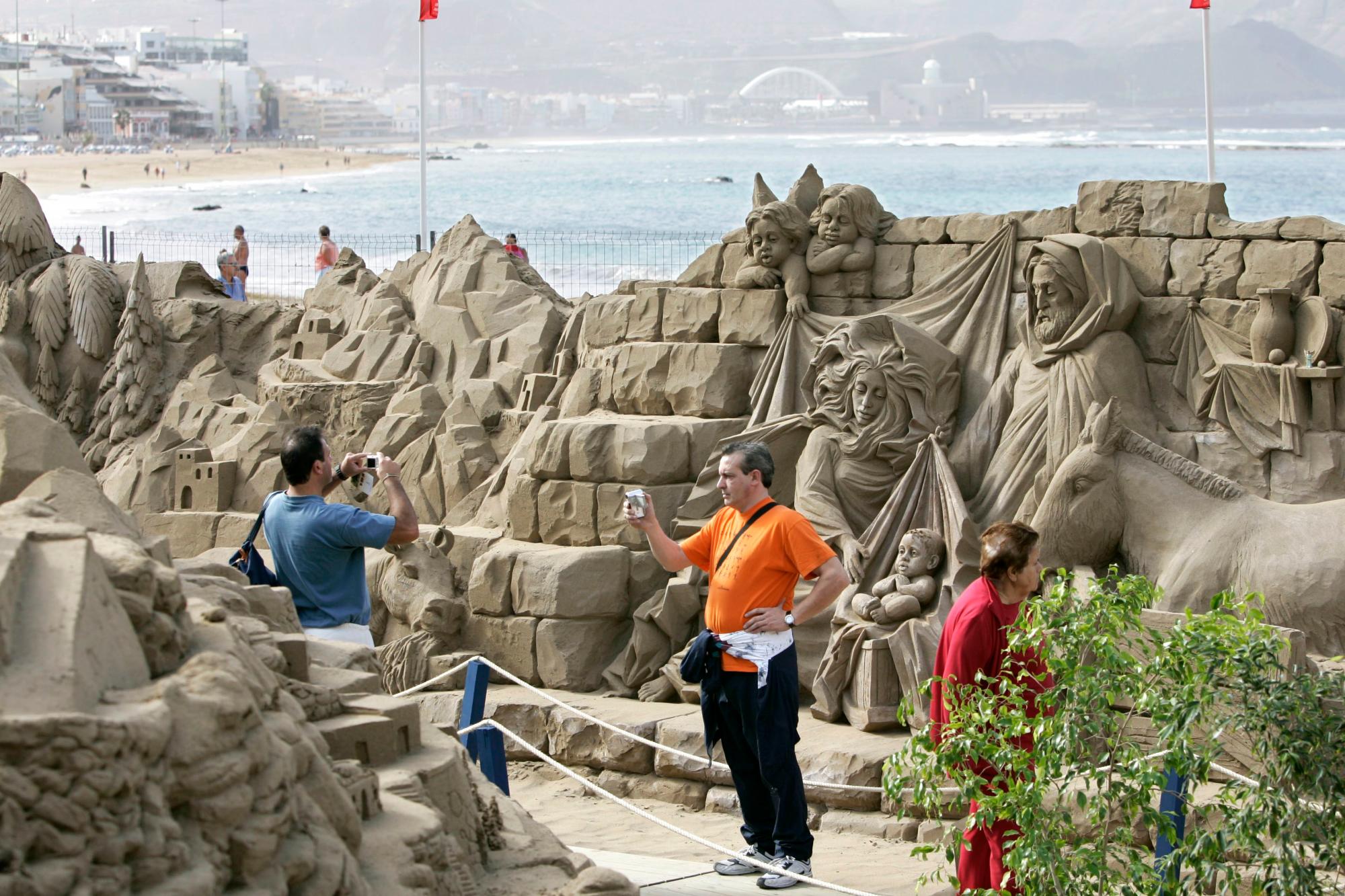 Varios turistas se hacen fotos en el mayor belén de arena de Europa, en la playa de Las Canteras (Las Palmas de Gran Canaria), donde se han juntado ocho escultores de varios países para unir arte y tradición en esta espectacular obra.