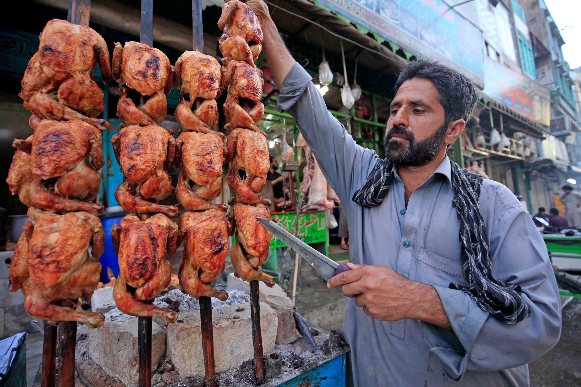Un hombre prepara pollos asados en un lado de la carretera durante el mes de ayuno islámico de Ramadán, en Peshawar (Pakistán). Los musulmanes de todo el mundo celebran el mes sagrado del Ramadán orando durante la noche y absteniéndose de comer, beber y actos sexuales durante el período entre el amanecer y el atardecer.