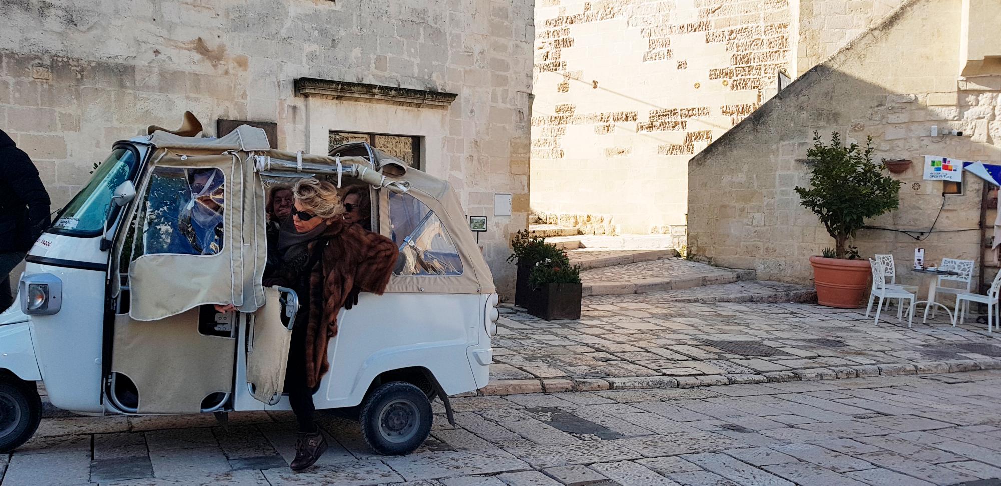 Una mujer baja de uno de los pequeños vehículos que recorren las laberínticas y estrechas calles de los  “Sassi“; de Matera.