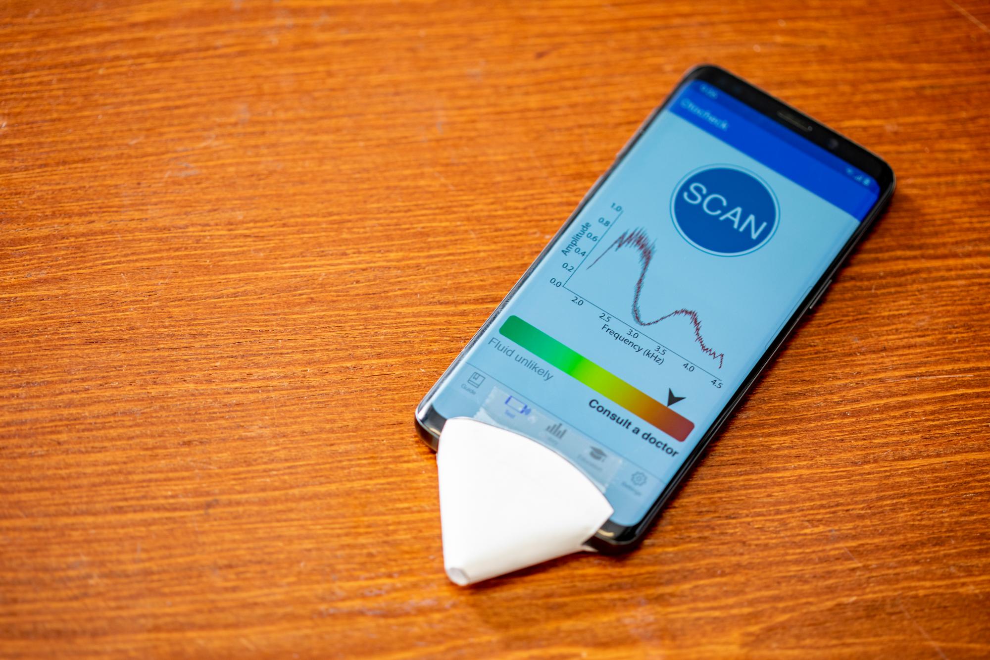 Los investigadores de UW han creado una nueva aplicación para teléfonos inteligentes que puede detectar el fluido detrás del tímpano. En la imagen el móvil con el pequeño cono de papel en la zona del micrófono.