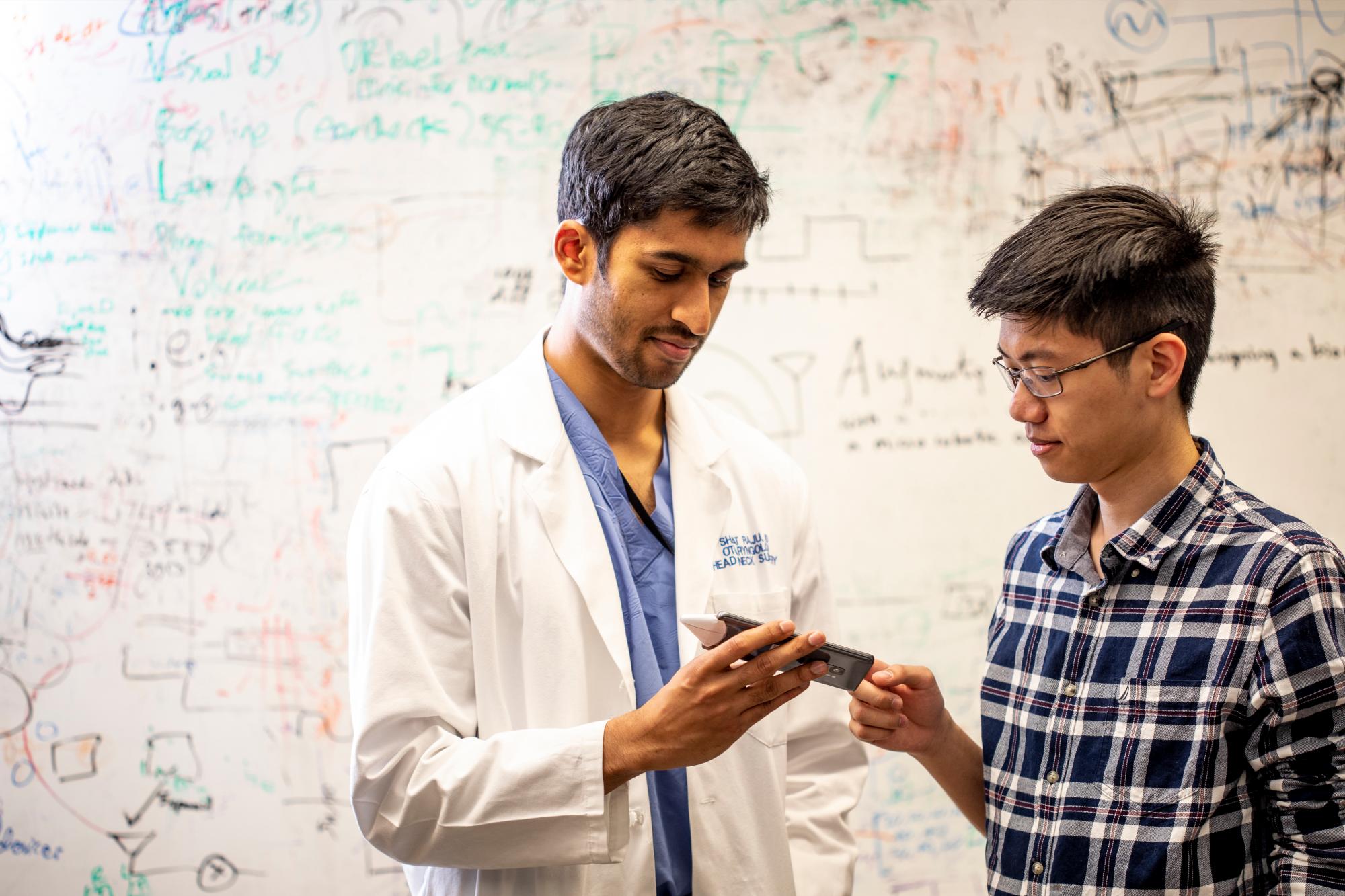 El Dr. Sharat Raju, residente quirúrgico en cirugía de otorrinolaringología de cabeza y cuello en la Escuela de Medicina de la Universidad de Washington (izquierda), y Justin Chan, estudiante de doctorado en la Escuela Allen, discuten la aplicación. 