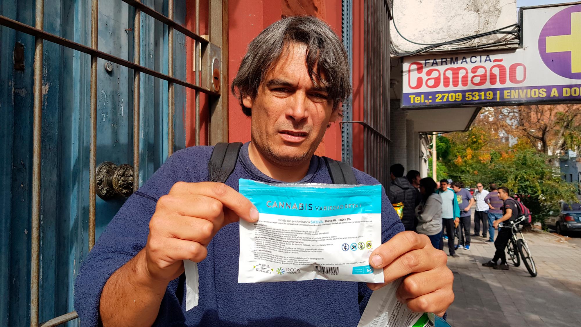 Borland muestra un paquete de marihuana recién comprado en una farmacia de Montevideo. Al fondo varios consumidores esperando su turno para adquirir el producto. 
