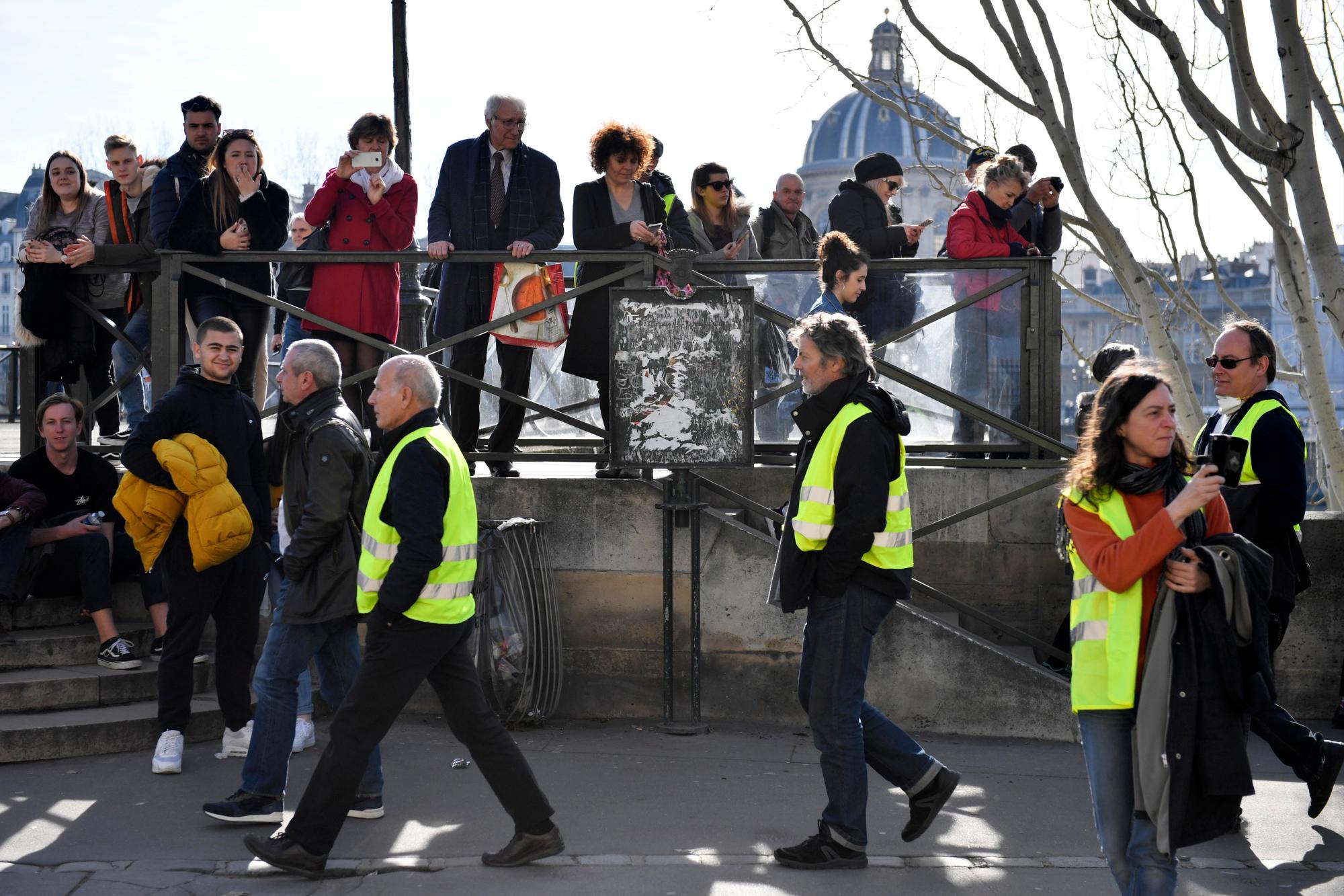París (Francia), 16/02/2019.- La gente mira a los manifestantes del movimiento ‘Gilets Jaunes’ (chalecos amarillos) caminando por el río Sena durante la manifestación del ‘Acto XIV’ (la 14a protesta nacional consecutiva en un sábado) en París, Francia, 16 de febrero de 2019. El llamado ‘Gilets Jaunes’ es un movimiento de protesta popular con partidarios de una amplia gama del espectro político, que originalmente comenzó con una protesta en todo el país a fines de 2018 contra los altos precios del combustible.