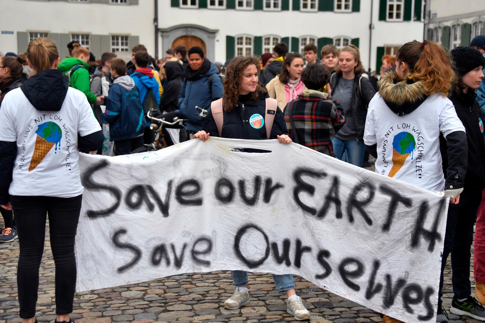 BASEL (SUIZA), 01/03/2019.- Tres jóvenes sujetan una pancarta en la que se lee la frase Salva nuestro planeta, salvémonos a nosotros mismos durante una manifestación contra el cambio climático, este viernes en Basel (Suiza). Protestas similares se han desarrollado a lo largo del día en otras ciudades europeas.