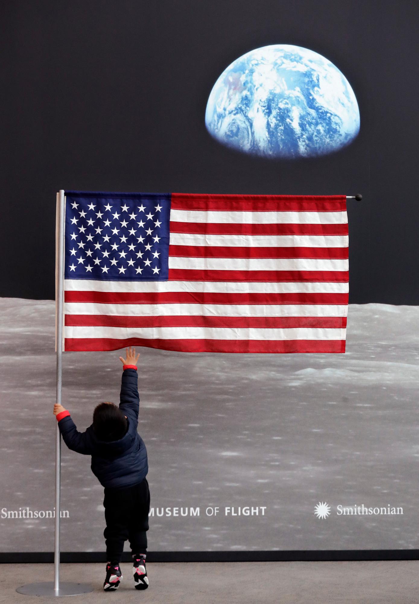 Guo JiuLe, 2, de Shanghai, China, alcanza una bandera estadounidense en la entrada de Destination Moon: La exhibición de la misión Apollo 11 en el Museo de Vuelo, antes de su apertura en Seattle.