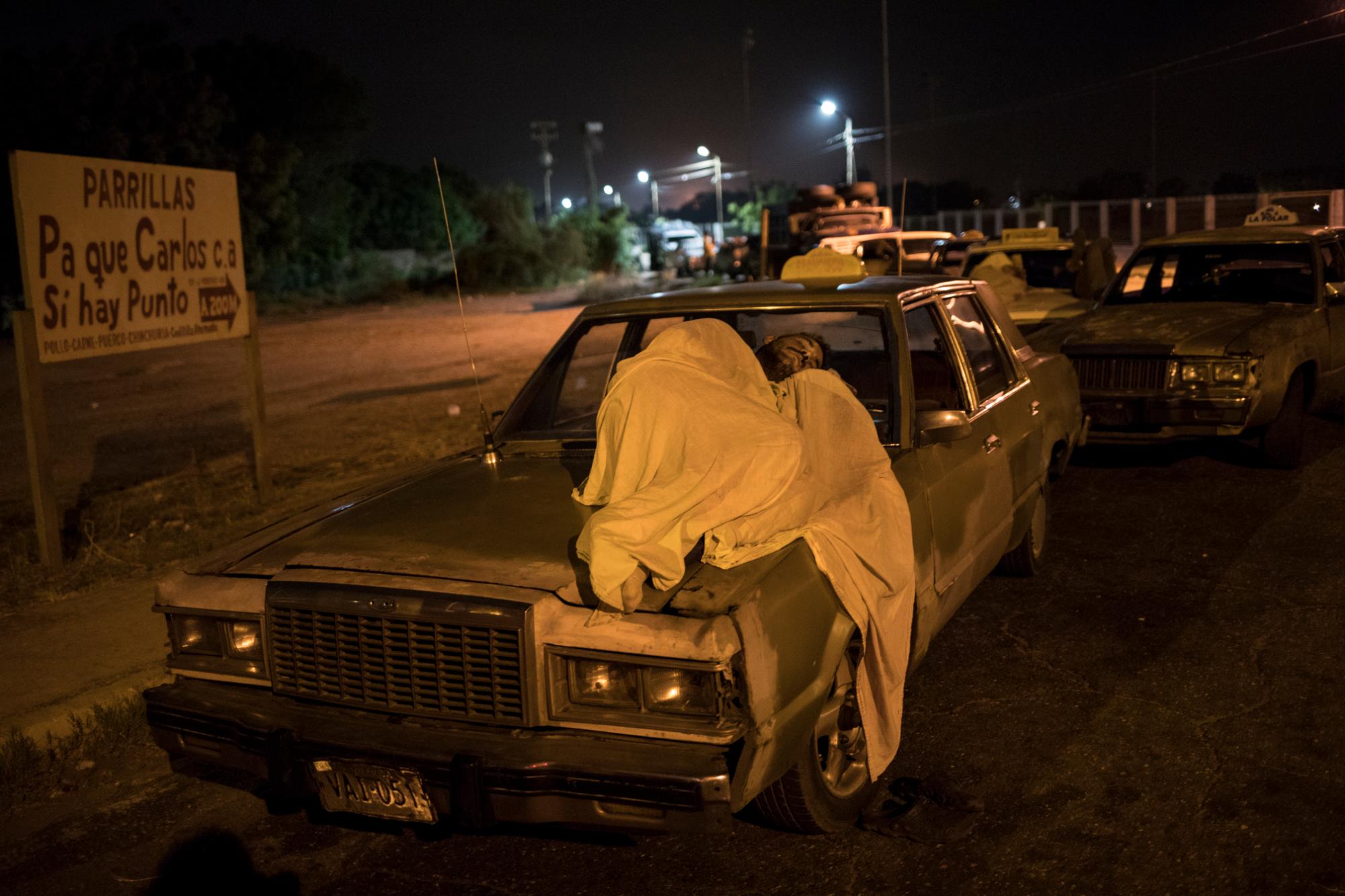 En la imagen, tomada el 23 de mayo de 2019, un hombre duerme sobre su auto mientras espera en una fila para obtener combustible, en Maracaibo, Venezuela. Como en otras ciudades, los cansados conductores duermen sobre sus autos mientras esperan la llegada del escaso combustible en largas filas en las gasolineras.