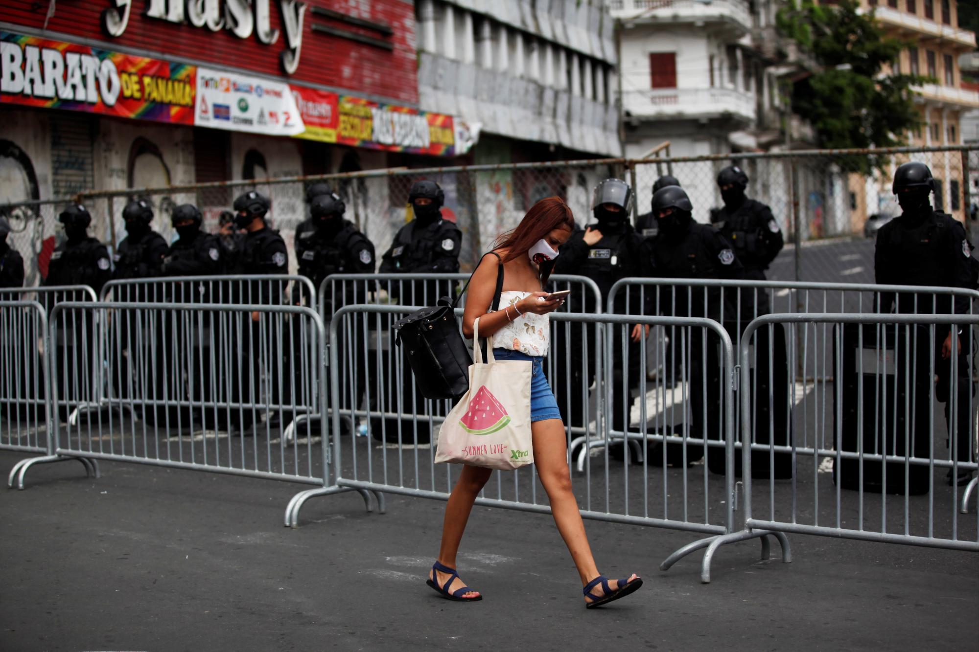 Una mujer protegida con tapabocas camina frente a un grupo de policías que resguarda las afueras de la Asamblea Nacional de Panamá este miércoles, en donde el presidente de la nación, Laurentino Cortizo, ofrece ante el parlamento su discurso por su primer año de mandato (EFE/ Bienvenido Velasco)