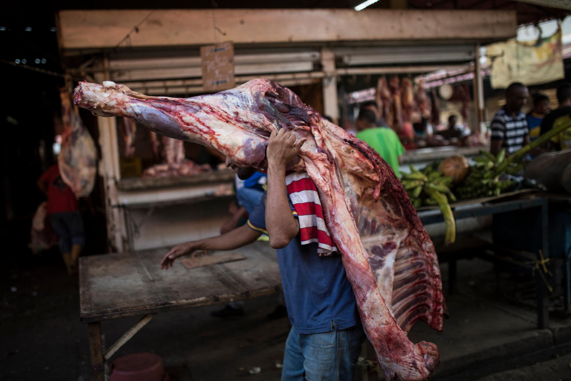 En la imagen, tomada el 16 de mayo de 2019, un vendedor carga con una pieza de carne en una carnicería en un mercado de Maracaibo, Venezuela. Tendrá que venderla pronto ya que, sin refrigeración, los alimentos perecederos se estropean rápidamente en las asfixiantes temperaturas de Maracaibo.