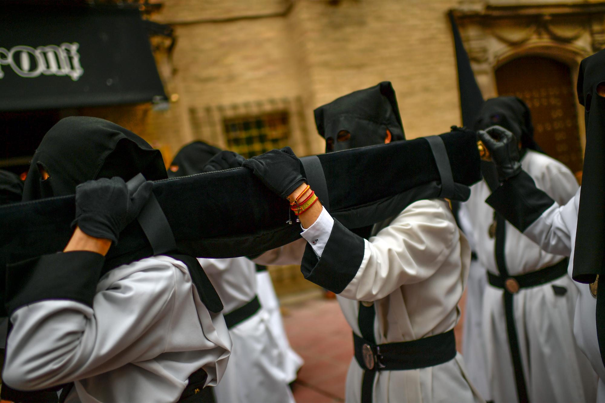 Penitentes encapuchados de la Hermandad ‘ ‘ Exaltación de la Santa Cruz ‘ ‘ participan en una procesión de la Semana Santa. Uno de ellos muestra un brazalete con colores nacionales, en Zaragoza, norte de España. 