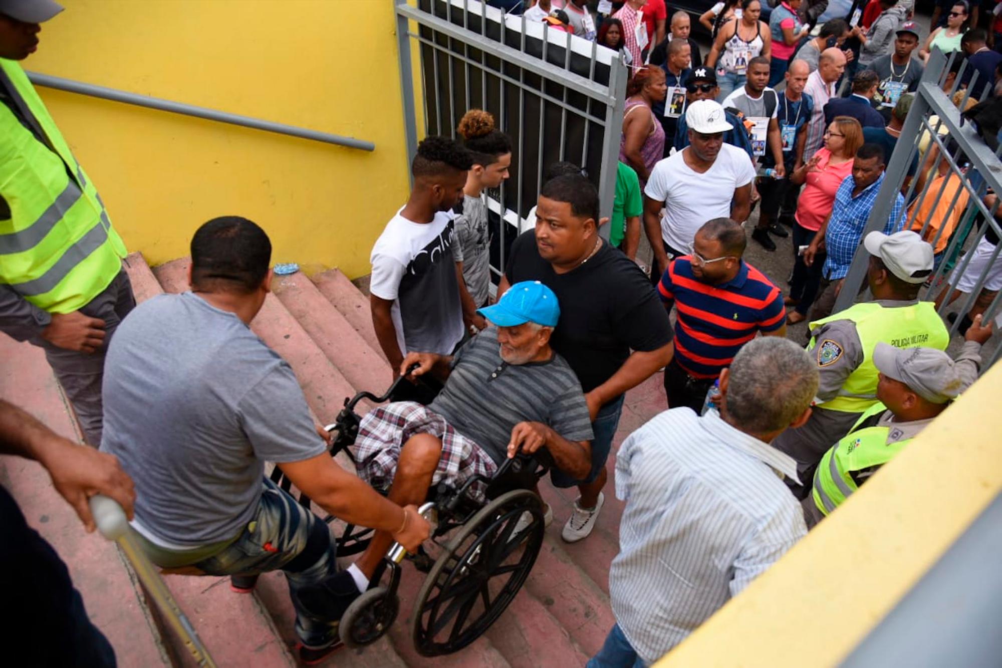 Un señor ayudado por otras personas, llega en silla de ruedas a ejercer su derecho al sufragio en el Club Gregorio Urbano Gilbert en el Ensanche Libertad, en el municipio de Santiago, cerca del mediodía de ayer domingo, antes de suspenderse las elecciones.