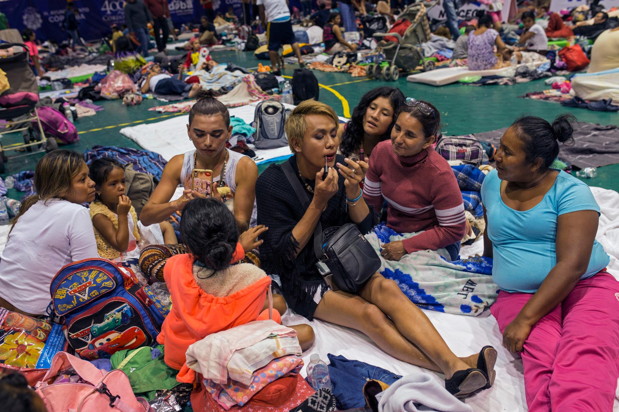 Dos mujeres transgénero se maquillan la cara en un refugio en Córdoba, México. Sobresaliendo entre la multitud por su brillante vestimenta y maquillaje, el grupo ha sufrido acoso verbal, especialmente por parte de hombres.