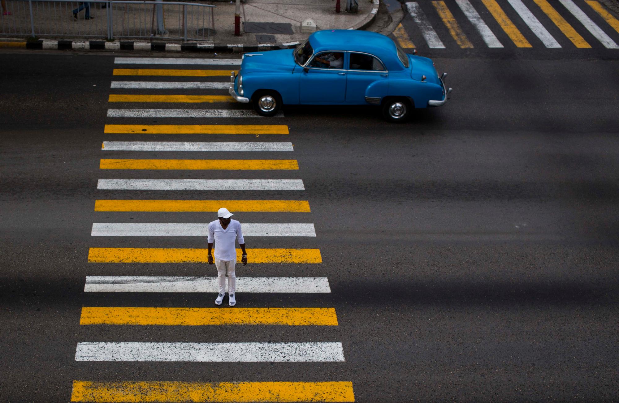Un hombre cruza una calle mientras pasa un automóvil clásico en La Habana, Cuba, el viernes 16 de noviembre de 2018. Cientos de automóviles clásicos se reunirán cerca del Malecón para honrar a este grupo único de vehículos, uno de los emblemas de Cuba.