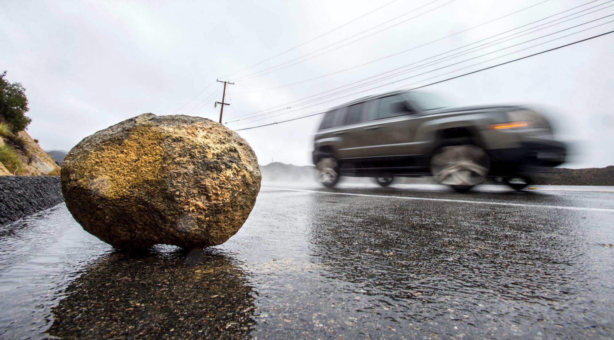 Un automóvil que viaja a lo largo de Santiago Canyon Road en Silverado Canyon pasa por una gran roca que cayó sobre la calzada el jueves por la mañana, 29 de noviembre de 2018, a medida que las fuertes lluvias y tormentas avanzaban por el Condado de Orange y el sur de California. Los meteorólogos dicen que el sistema meteorológico que ha estado lloviendo todo el día en el sur de California ha desarrollado inestabilidad y puede producir tormentas eléctricas.