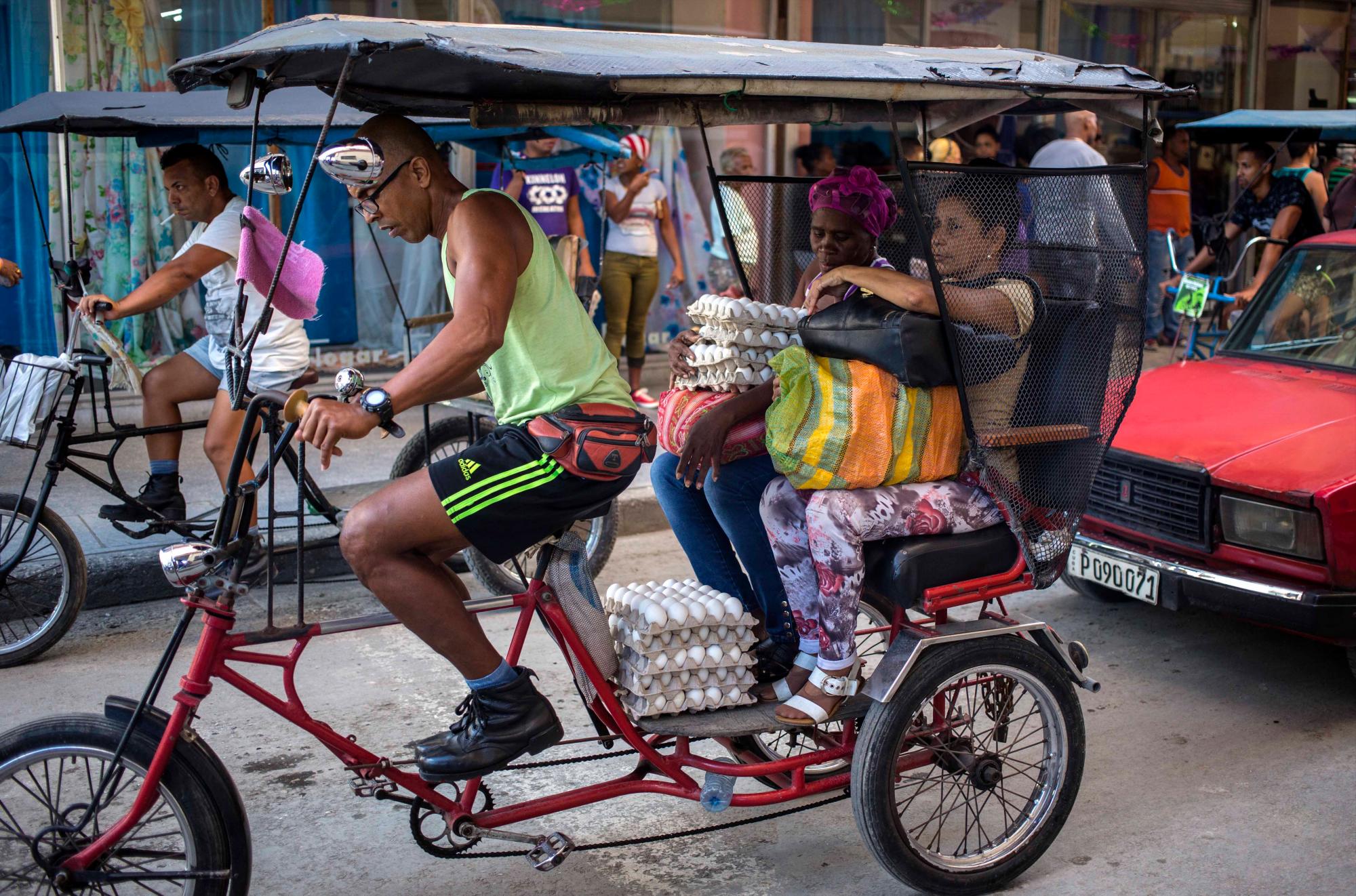 Un conductor de taxi en bicicleta ofrece transporte a las mujeres que recién compraron docenas de huevos en La Habana, Cuba, el jueves 6 de diciembre de 2018.
