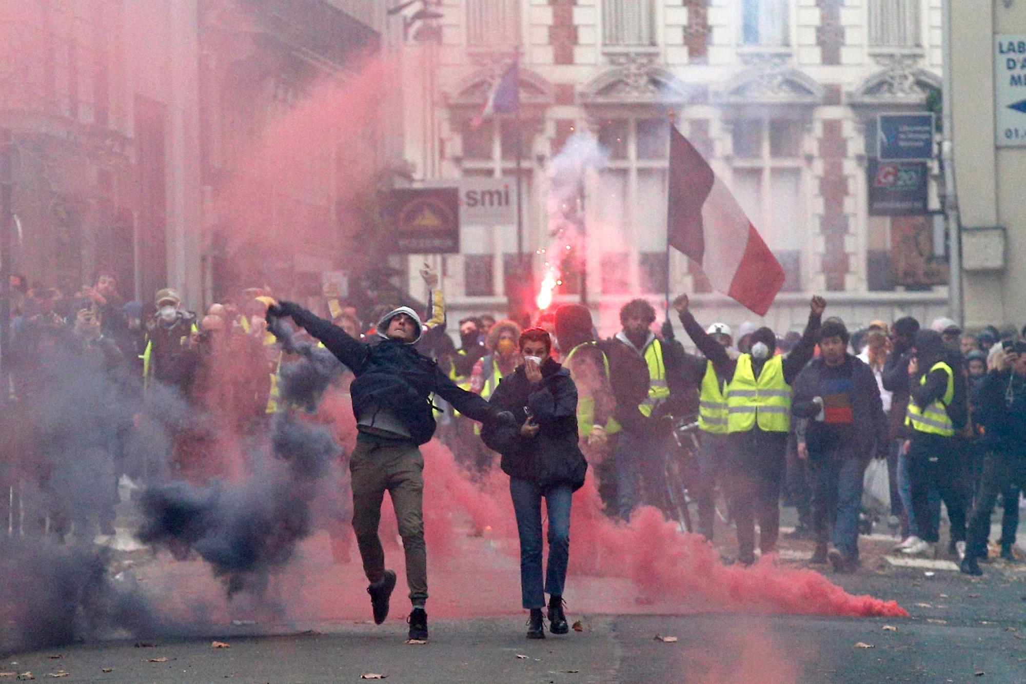 Los manifestantes lanzan objetos y devuelven las bombas de gases lacrimógenos lanzadas por la policía antimotines en la Avenida de Los Campos Eliseos de París, Francia.