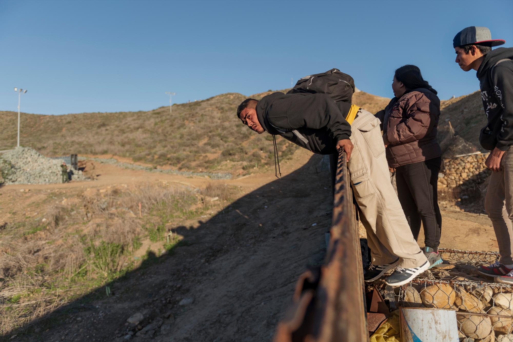 Migrantes procedentes de Honduras chequean la vigilancia antes de saltar la valla fronteriza y cruzar al lado de Estados Unidos.