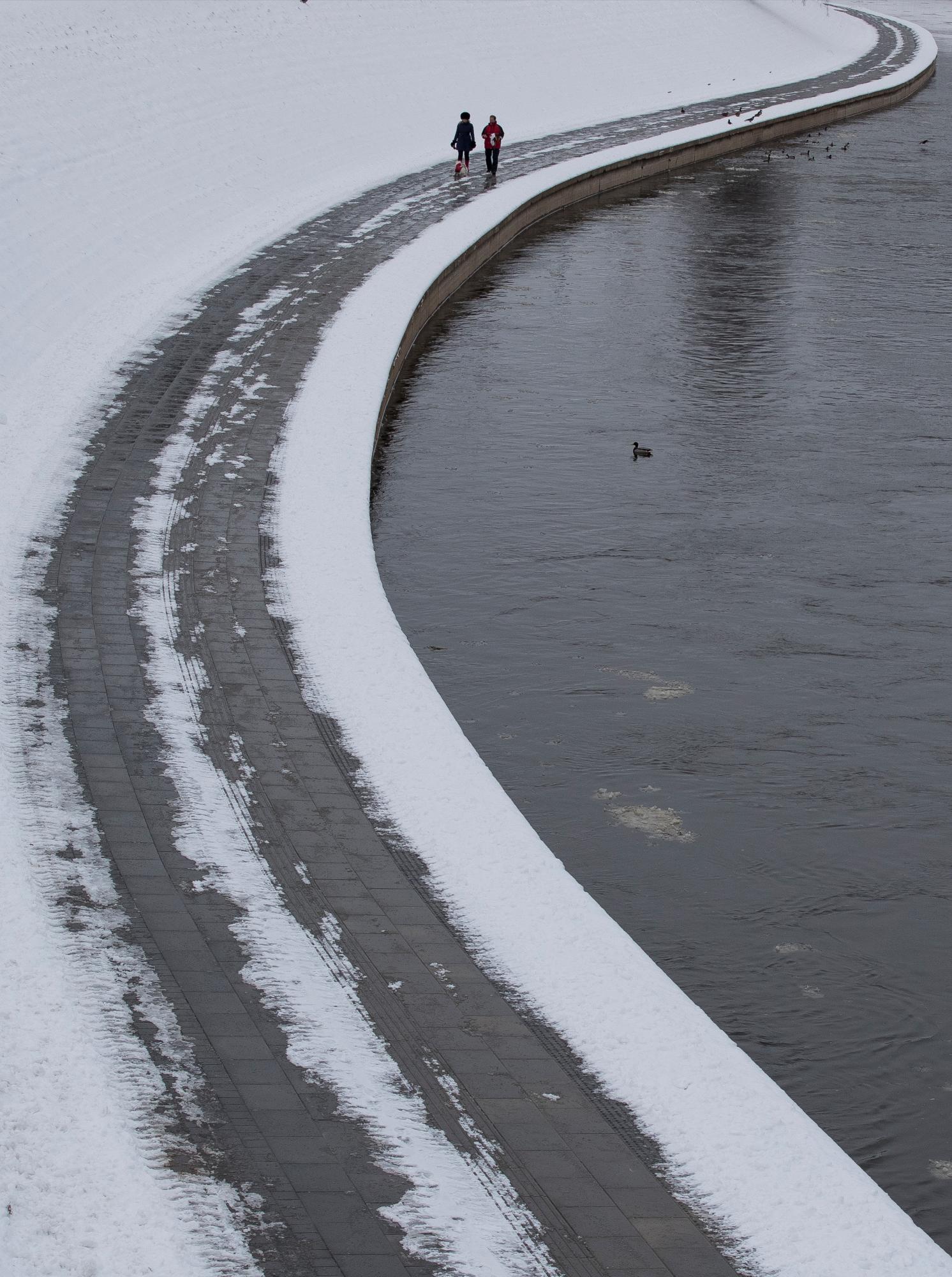 Una pareja pasea a un perro a lo largo de las orillas del río Neris en Vilnius, Lituania, sábado 5 de enero de 2019. Los residentes de la capital lituana están disfrutando de los días nevados de invierno, con temperaturas de apenas 3 grados centígrados (26.6 grados Fahrenheit).
