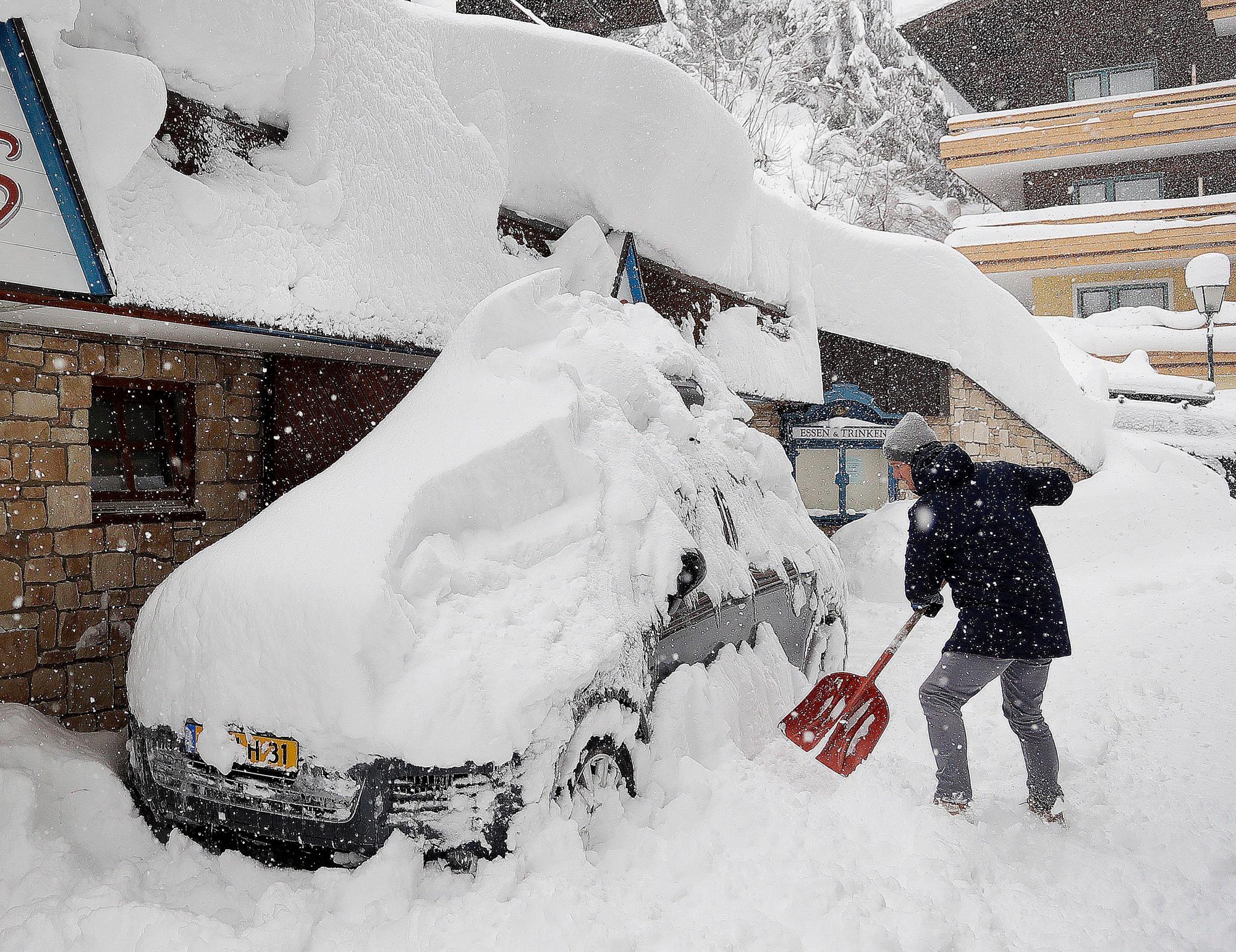Un turista de esquí retira las espumas de nieve de automóviles después de que caigan fuertes nevadas en Filzmoos, Austria, sábado 5 de enero de 2019.