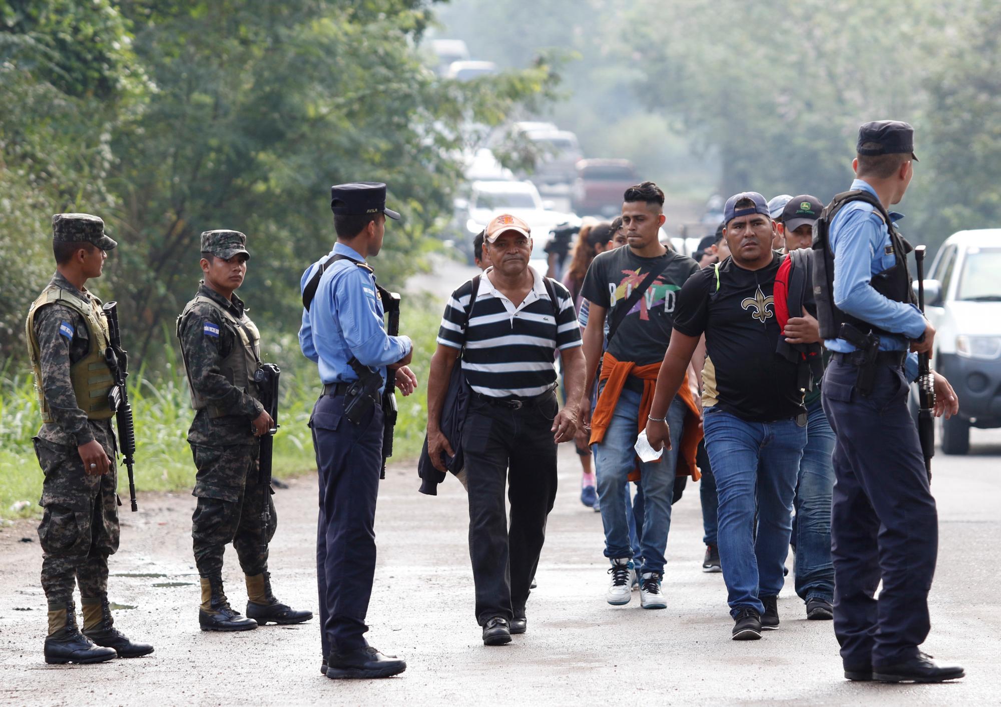 Los migrantes que se dirigen a Estados Unidos pasan por delante de las fuerzas de seguridad que detienen algunos vehículos que transportan a migrantes para revisar sus documentos en Cofradía, Honduras.