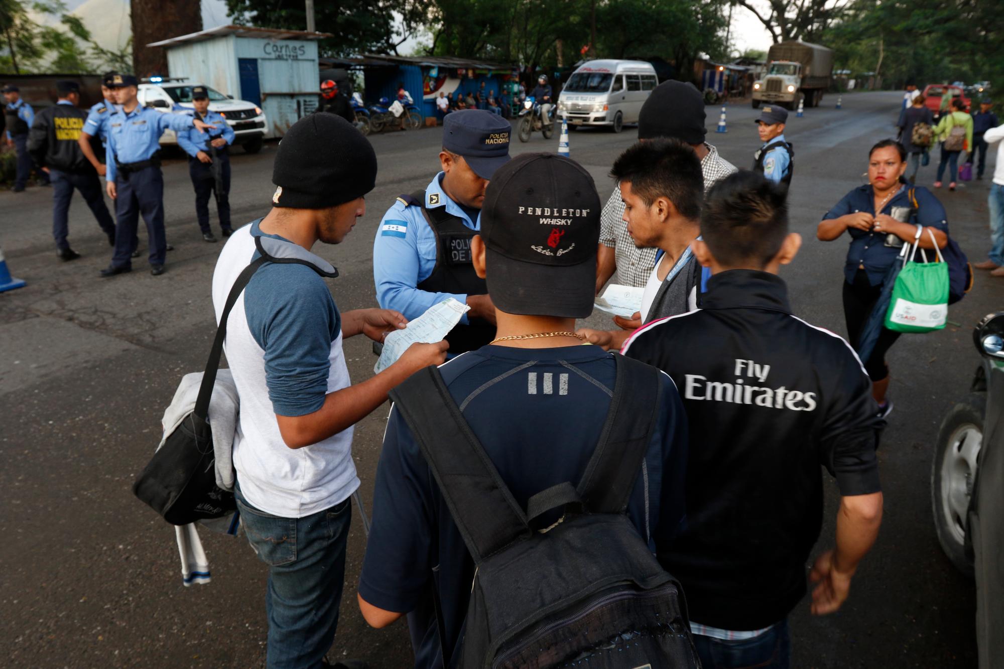 La policía local verifica los documentos de algunos migrantes que se dirigen a la lejana frontera de los EE. UU., al pasar por Cofradía, Honduras.
