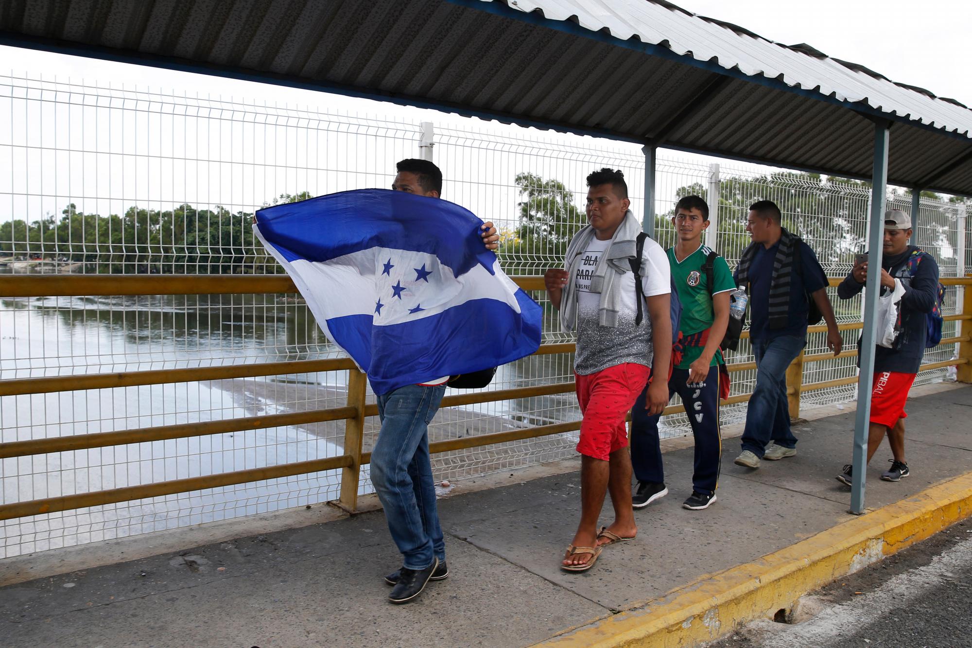 Los hombres cruzan el puente del río Suchiate con una bandera hondureña mientras cruzan la frontera hacia México desde Guatemala, cerca de Ciudad Hidalgo, estado de Chiapas, México, el jueves 17 de enero de 2019. Cientos de migrantes centroamericanos caminan y hacen autostop a través de la región. como parte de una nueva caravana de migrantes que esperan llegar a los Estados Unidos.