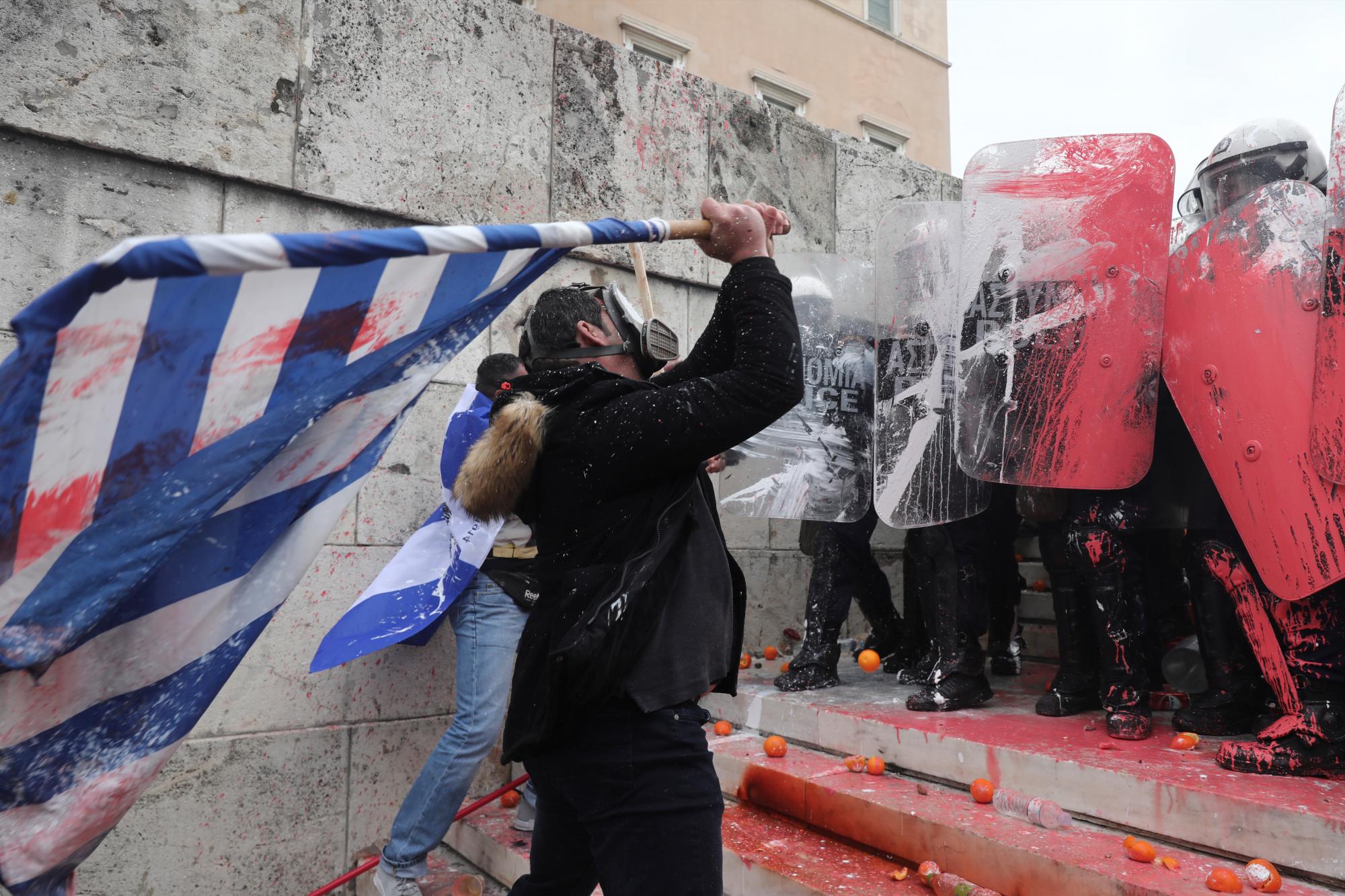 Un manifestante usa la bandera griega para combatir a la policía antidisturbios durante un mitin en Atenas, el domingo 20 de enero de 2019.
