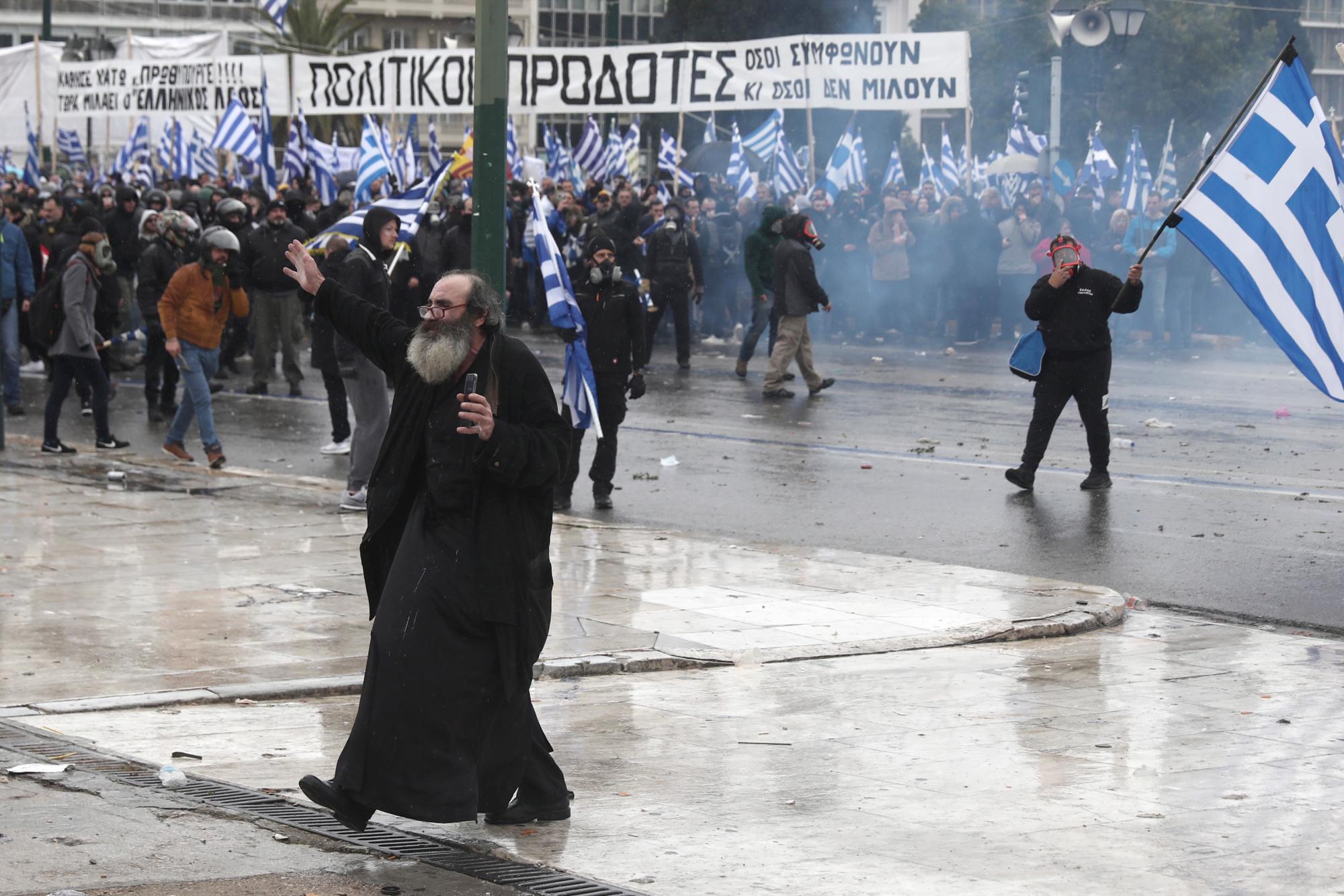 Un monje hace un gesto después de que la policía antidisturbios griega lanzara gas lacrimógeno durante un mitin en Atenas, el domingo 20 de enero de 2019.