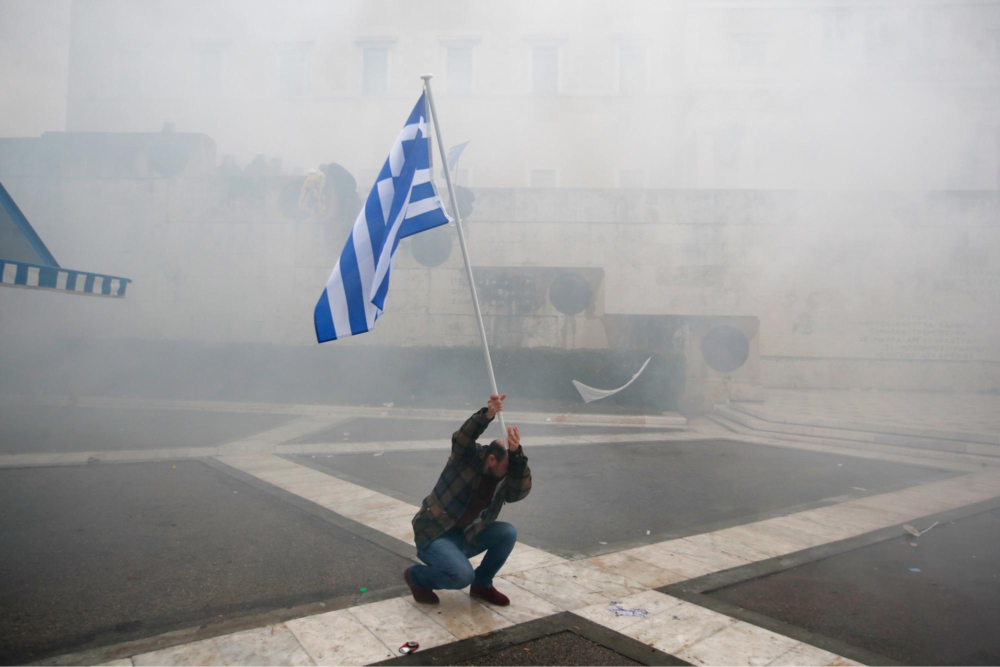 Un manifestante solitario sostiene la bandera griega mientras se sumerge en una nube de gas lacrimógeno durante los enfrentamientos después de un mitin en Atenas, el domingo 20 de enero de 2019. El Parlamento de Grecia votará la próxima semana si ratifica el acuerdo que cambiará el  nombre de su vecino del norte,  Macedonia del Norte.