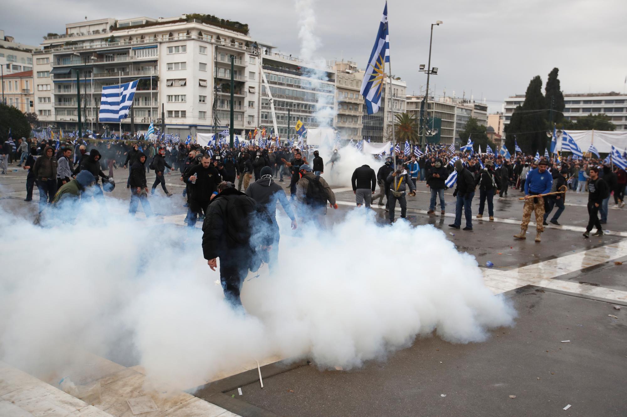 Los manifestantes con banderas griegas se retiran después de que la policía antidisturbios lanzara gas lacrimógeno durante los enfrentamientos después de un mitin en Atenas, el domingo 20 de enero de 2019.