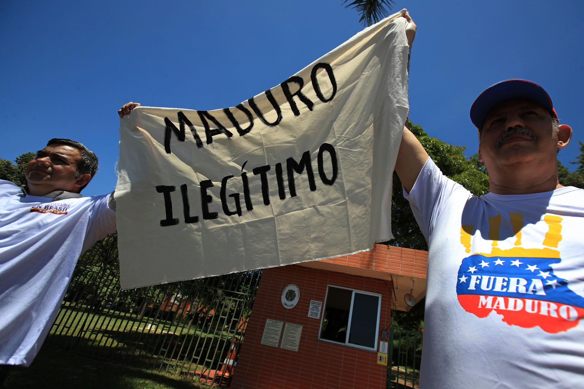 Los ciudadanos venezolanos que viven en Brasil sostienen un pedazo de tela con un mensaje que se lee en español; “Maduro ilegítimo” durante una protesta contra el gobierno del presidente Nicolas Maduro, frente a la embajada de Venezuela en Brasilia, Brasil, miércoles 23 de enero de 2019.