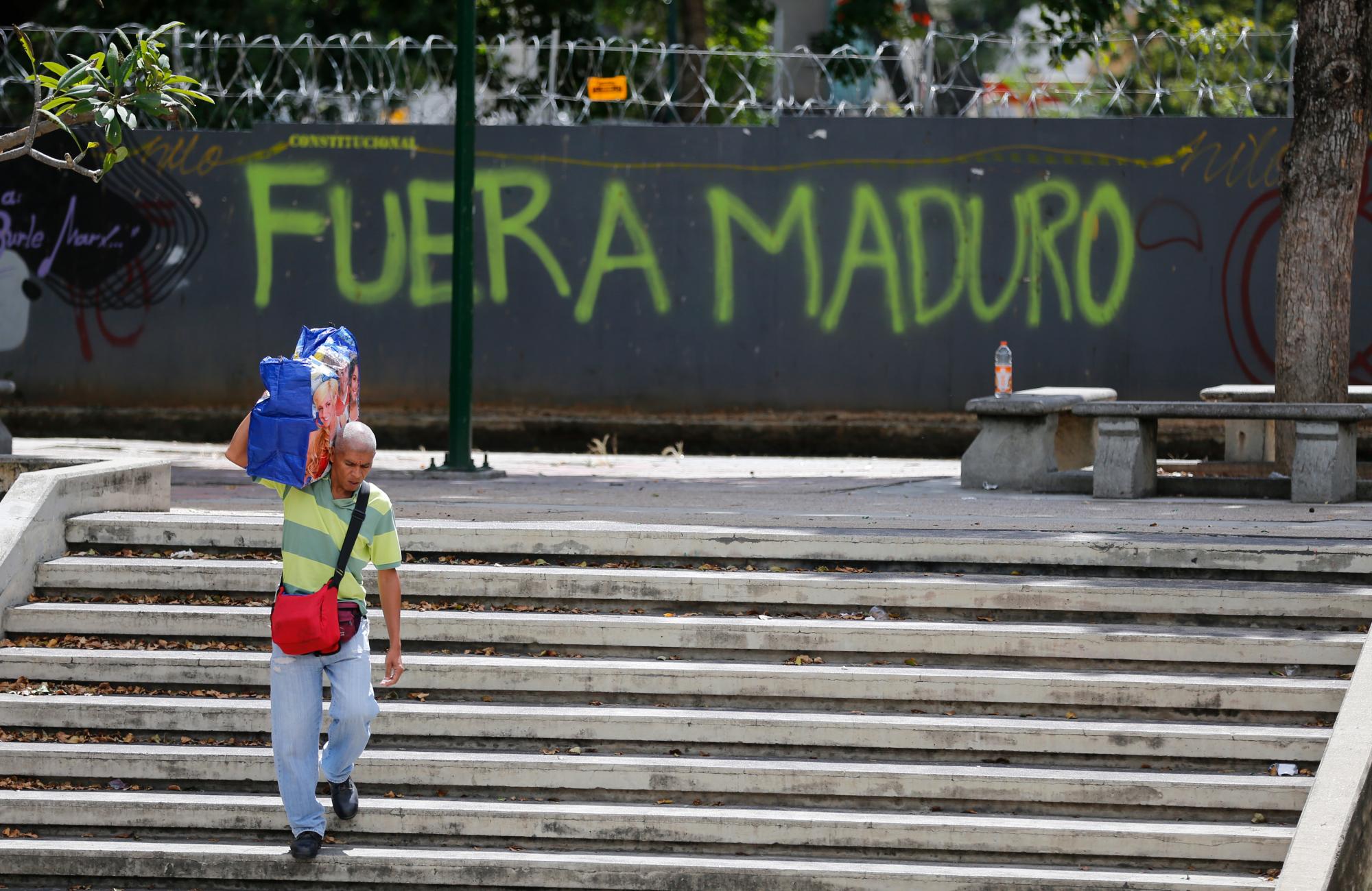 Un hombre pasa frente a los graffitis en la pared de un lote baldío que dice en español: “Salga de Maduro”, refiriéndose al presidente Nicolas Maduro en Caracas, Venezuela, jueves 24 de enero de 2019.  y Maduro entablando una pelea con el gobierno de Trump.