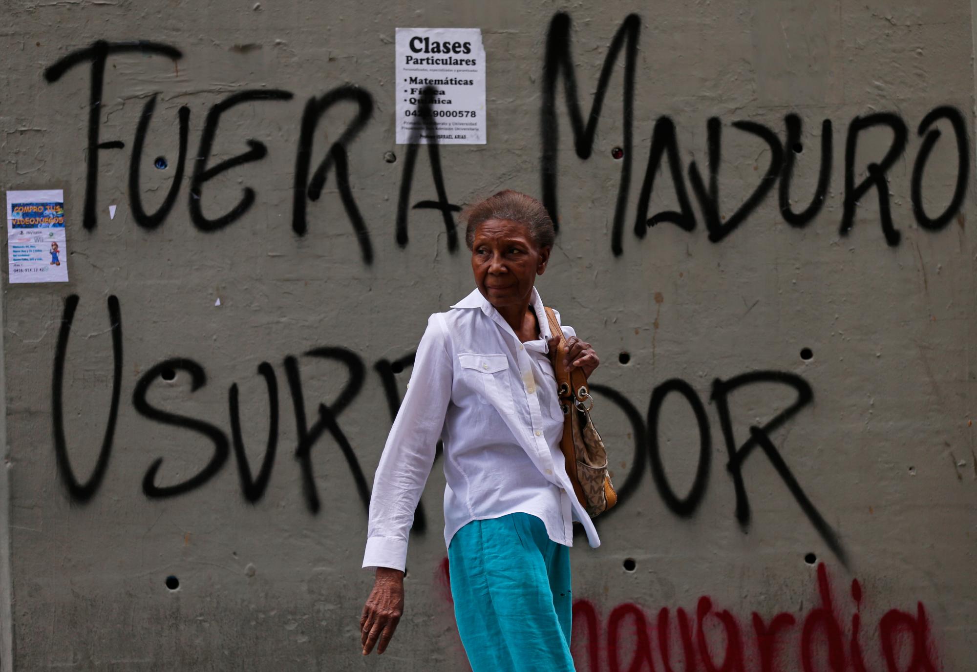 Una mujer camina frente a un muro con el mensaje: Fuera Maduro usurpador en referencia al presidente Nicolás Maduro en Caracas, Venezuela, el jueves 24 de enero de 2019.