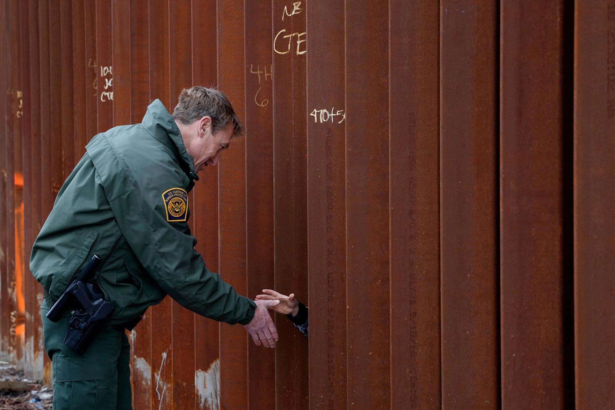 Rodney Scott, el jefe del sector de la patrulla fronteriza de San Diego, saluda con sus manos a través de una sección de muro fronterizo recién reemplazado en San Diego. Scott dijo que la patrulla fronteriza tenía que empezar en algún lugar, y San Diego era el corredor más concurrido para los cruces ilegales en la mayoría de los años noventa.