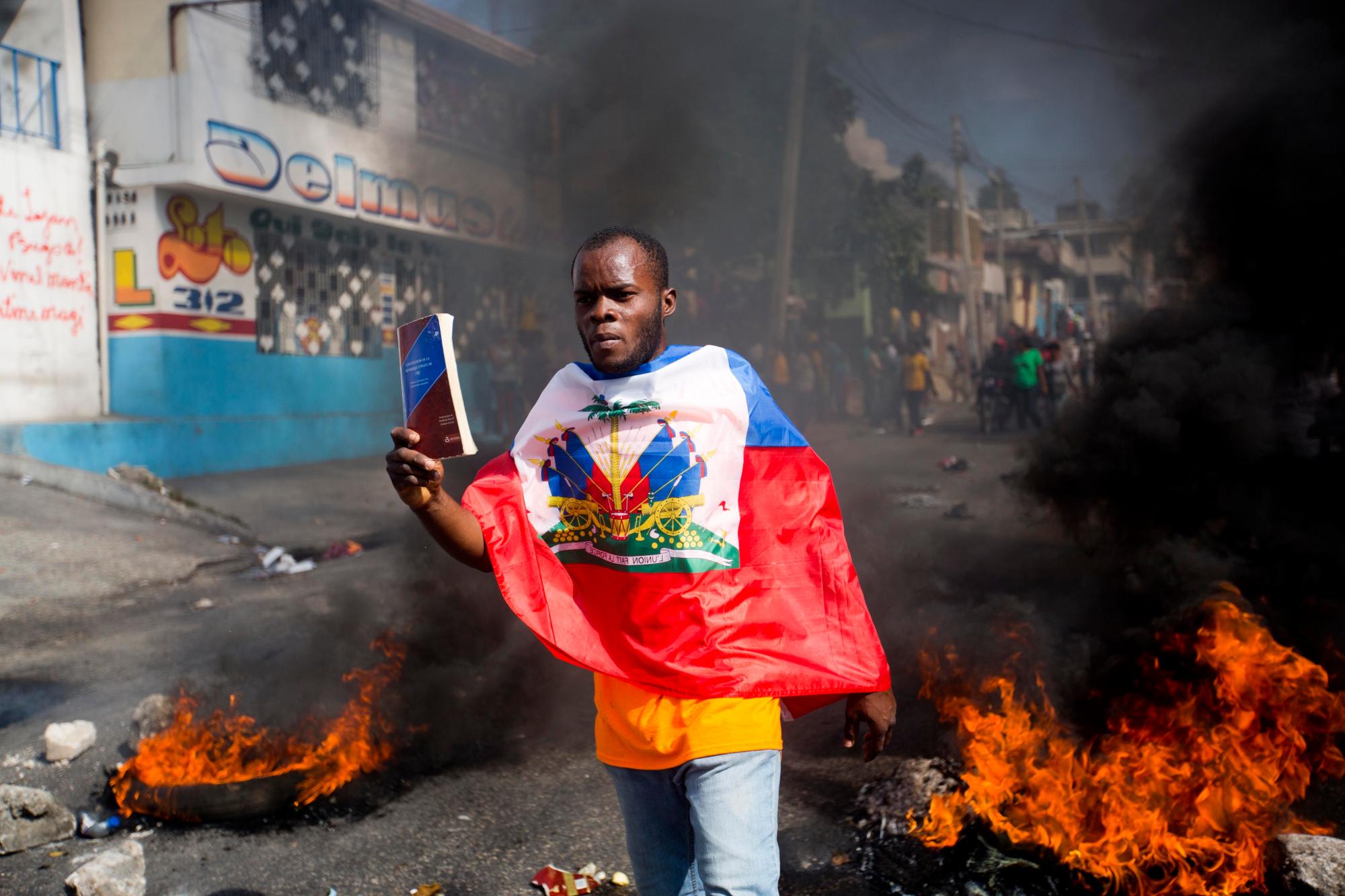 Un manifestante envuelto en la bandera haitiana, sostiene una copia de la constitución haitiana, durante una protesta para exigir la renuncia del presidente Jovenel Moise y exigir saber cómo los fondos de Petro Caribe han sido utilizados por las administraciones actuales y pasadas, en Port-au. -Prince, Haití, jueves 7 de febrero de 2019. Gran parte del apoyo financiero para ayudar a Haití a reconstruirse después del terremoto de 2010 proviene del fondo venezolano Petro Caribe, un pacto de 2005 que otorga a los proveedores financiamiento por debajo del mercado para el petróleo y está bajo control. del gobierno central.