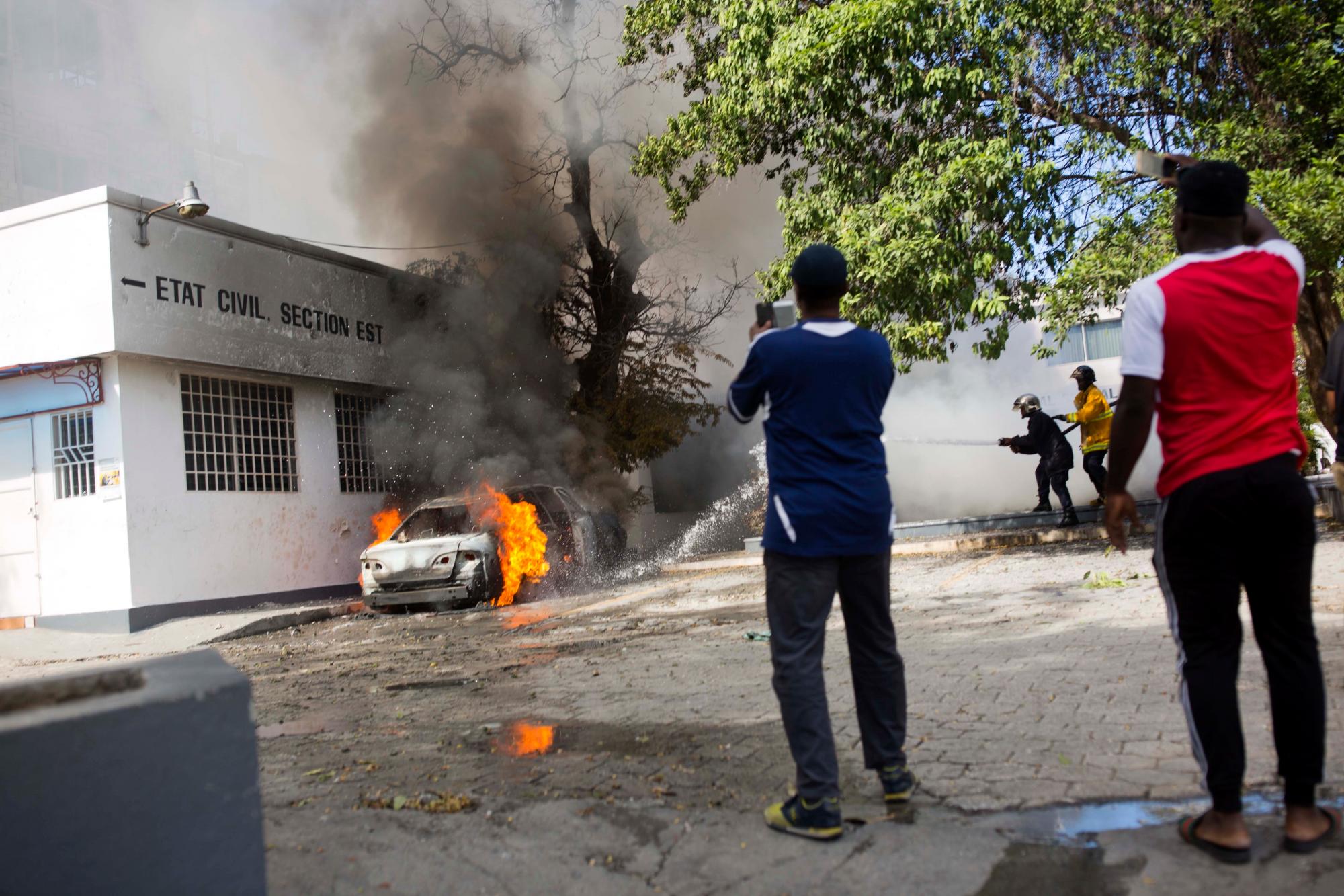 Los bomberos apagan un incendio en un automóvil quemado por manifestantes que exigen la renuncia del presidente Jovenel Moïse, fuera de la sede de protección ciudadana OPC del gobierno en Puerto Príncipe, Haití.