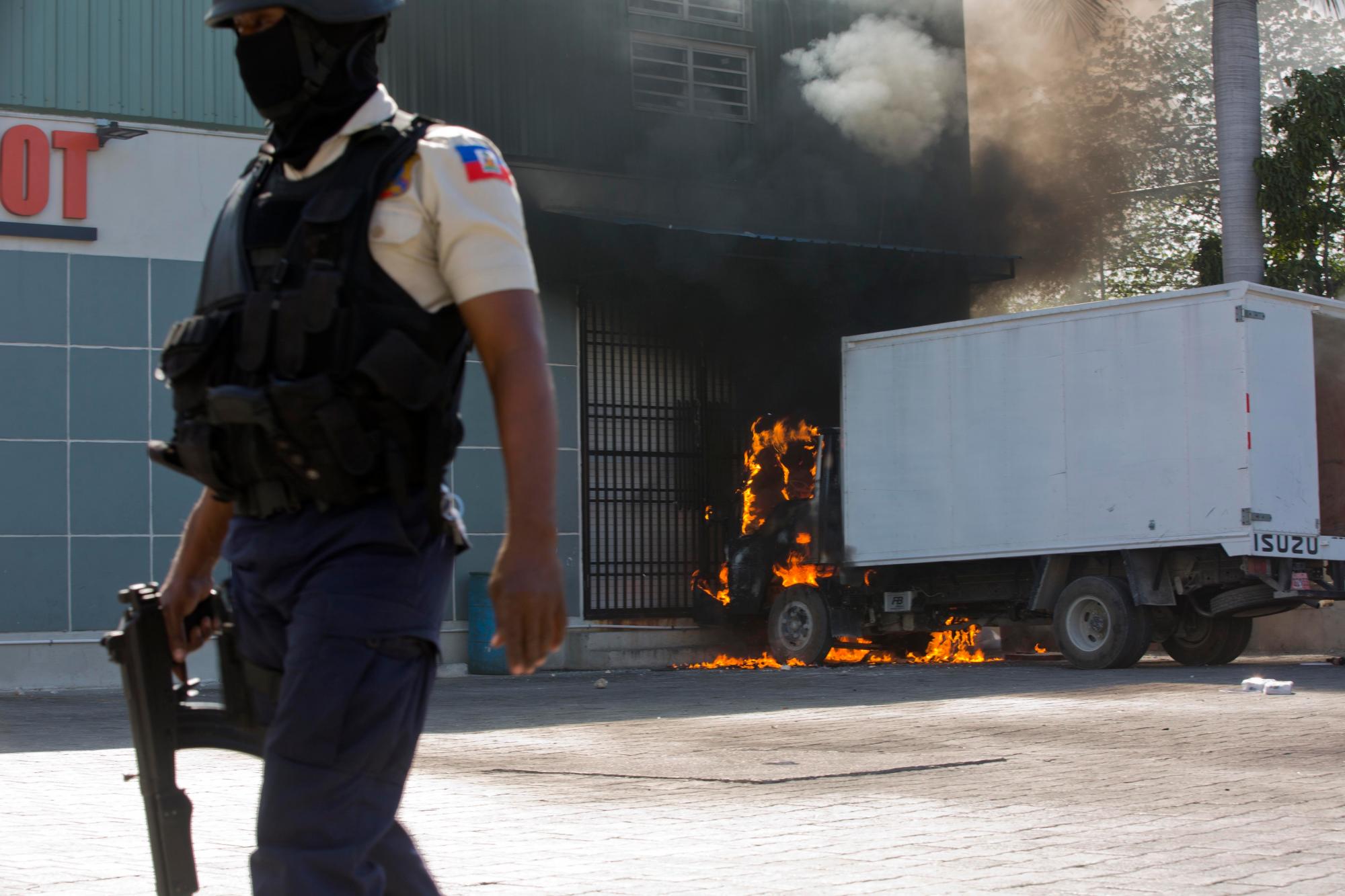 Un oficial de la policía nacional enmascarado patrulla cerca de un camión que se incendió durante una protesta para exigir la renuncia del presidente Jovenel Moïse en Puerto Príncipe, Haití.