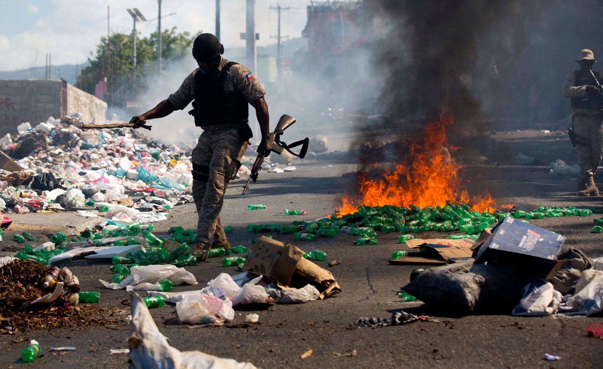 Un oficial de la policía nacional intenta despejar un bloque de carreteras incendiado por los manifestantes que exigen la renuncia del presidente Jovenel Moïse en Puerto Príncipe, Haití.