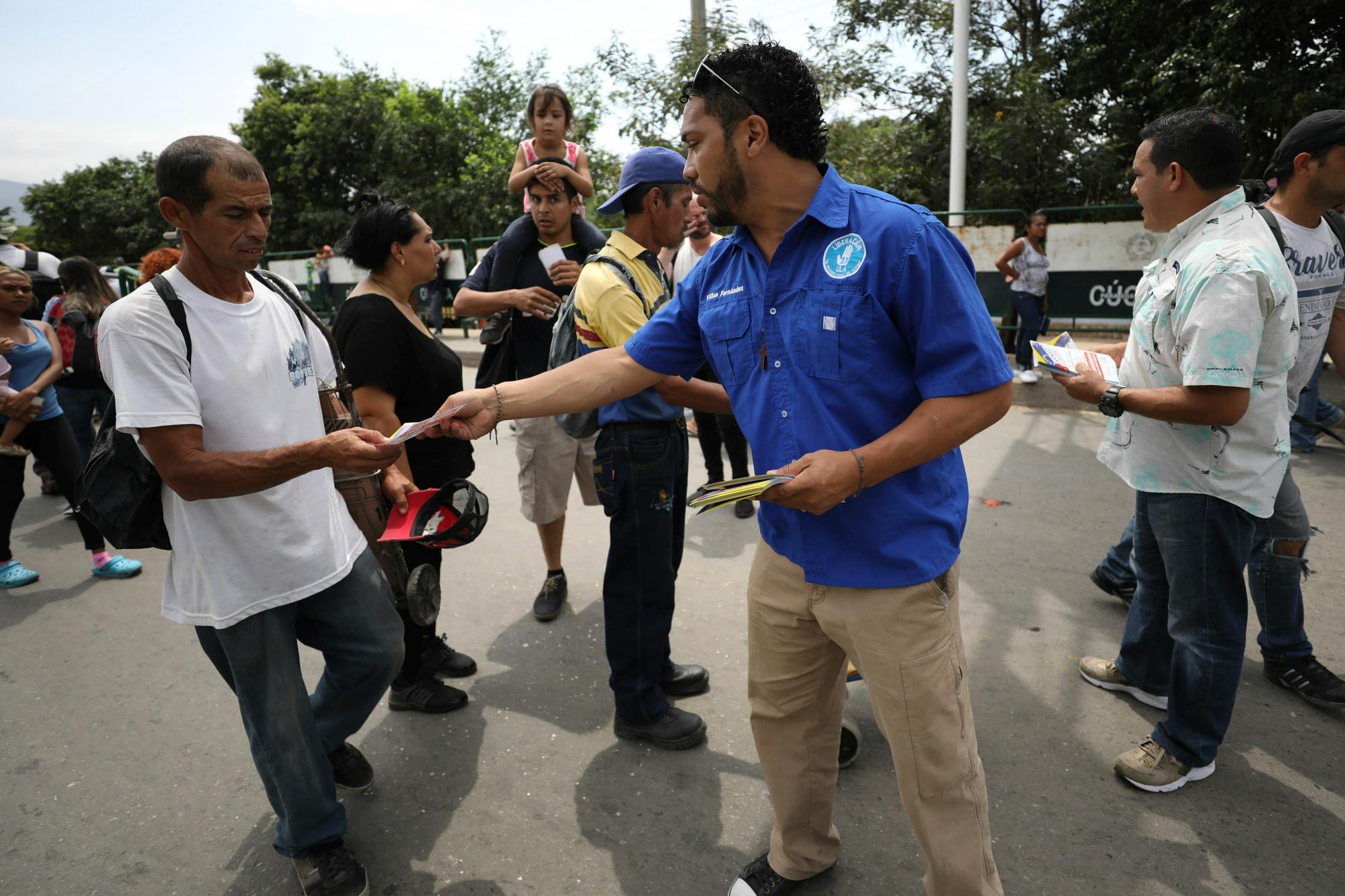 Políticos venezolanos exiliados, a la derecha, repartidor de volantes invitando a migrantes venezolanos a salir a las calles el 23 de febrero para apoyar la entrega de ayuda planificada a Venezuela, en la parada, en la frontera con Venezuela, Colombia.