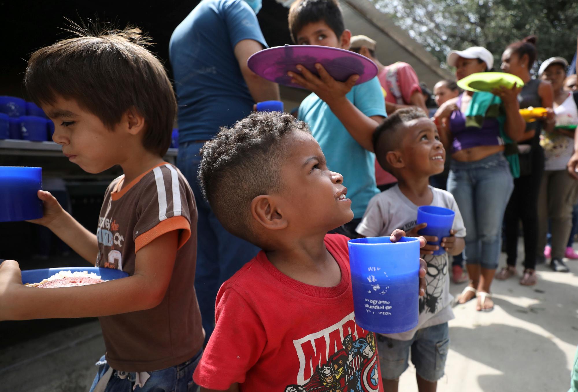 Niños venezolanos sostienen vasos llenos de jugo de uva durante el almuerzo.