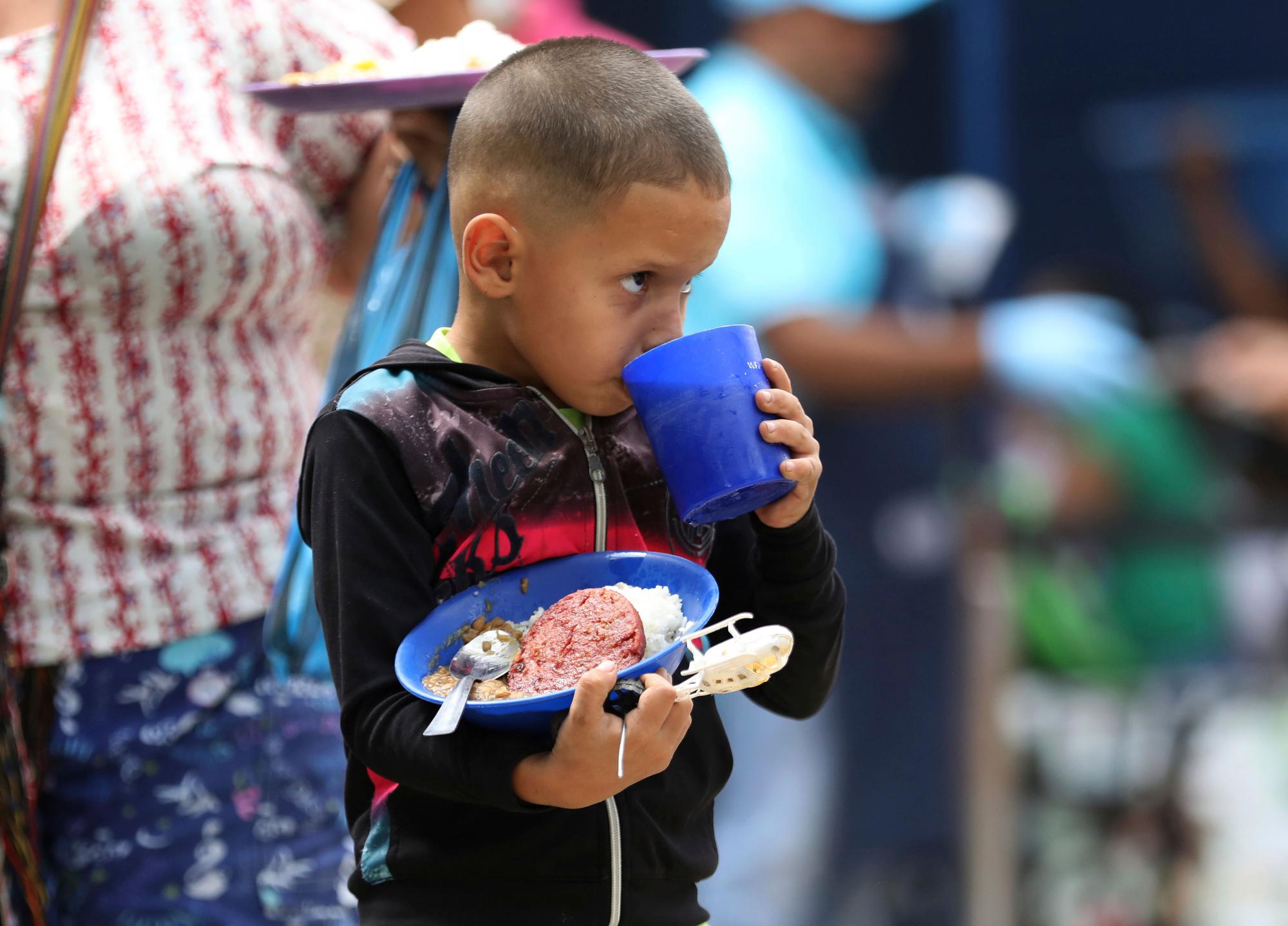 Un niño toma un sorbo de refresco de uva mientras disfruta su almuerzo en el refugio.
